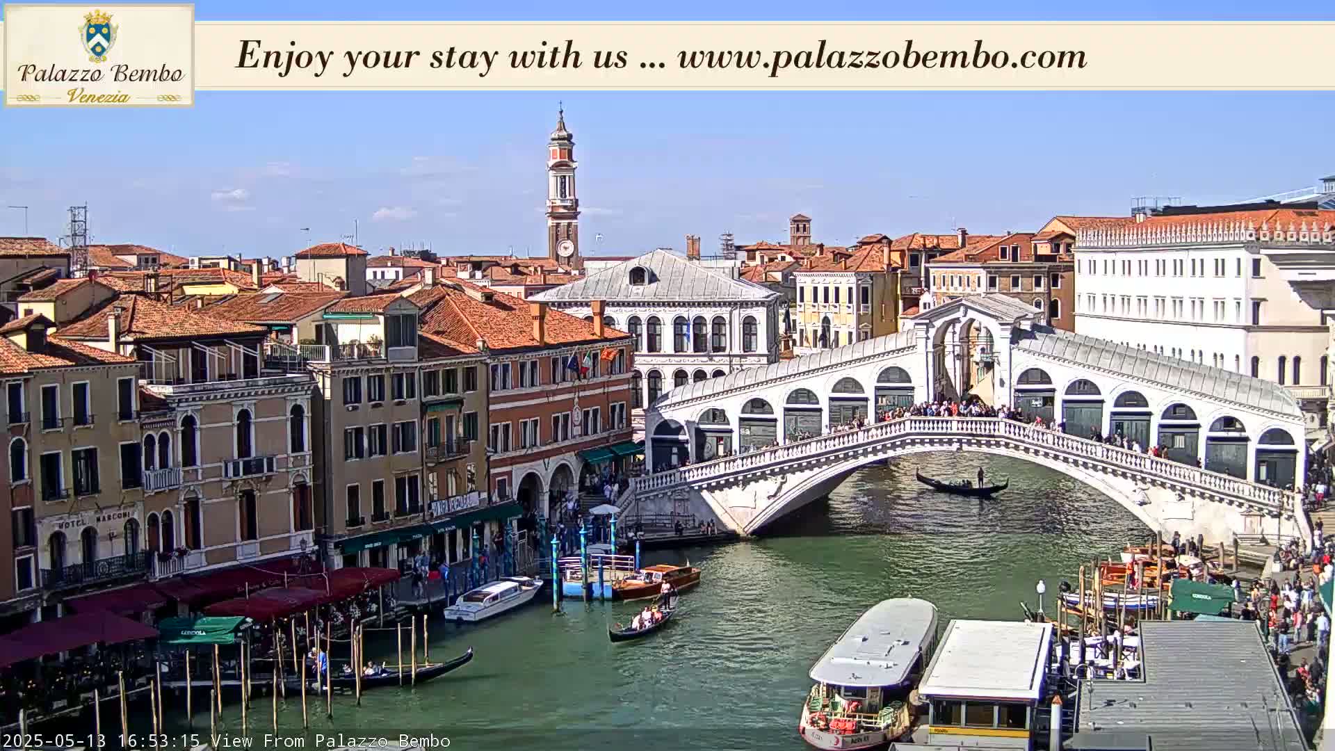 A sunny Venetian cityscape features a canal with gondolas, boats, and the Rialto Bridge filled with pedestrians, all surrounded by historic buildings.