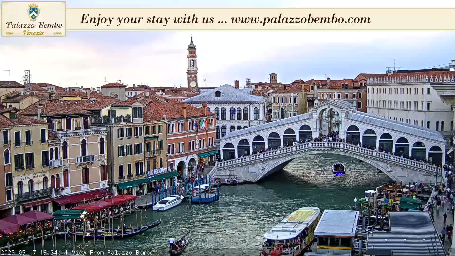A bridge spans a canal in Venice, with numerous boats and gondolas below, under a partly cloudy sky.