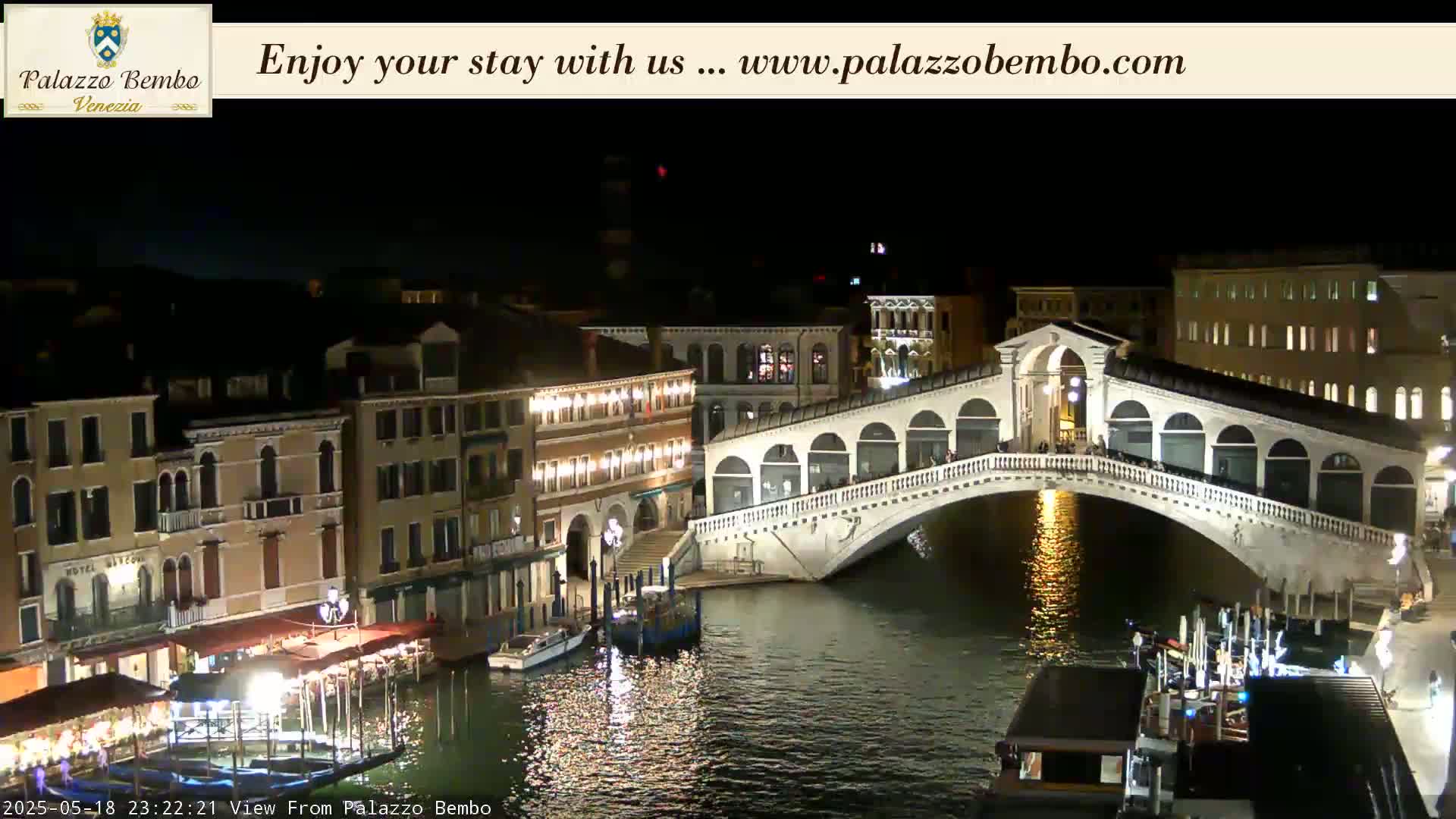 A nighttime view of a canal in Venice, showing a lit-up bridge and buildings along the waterway.