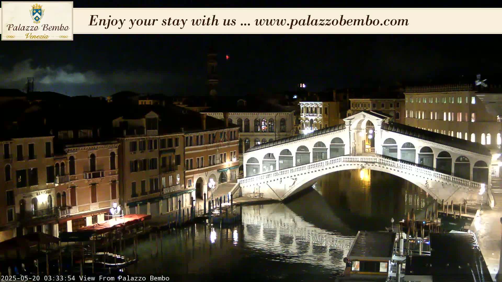 A nighttime view of a canal in Venice, showing a bridge and buildings along the waterfront under a partly cloudy sky.