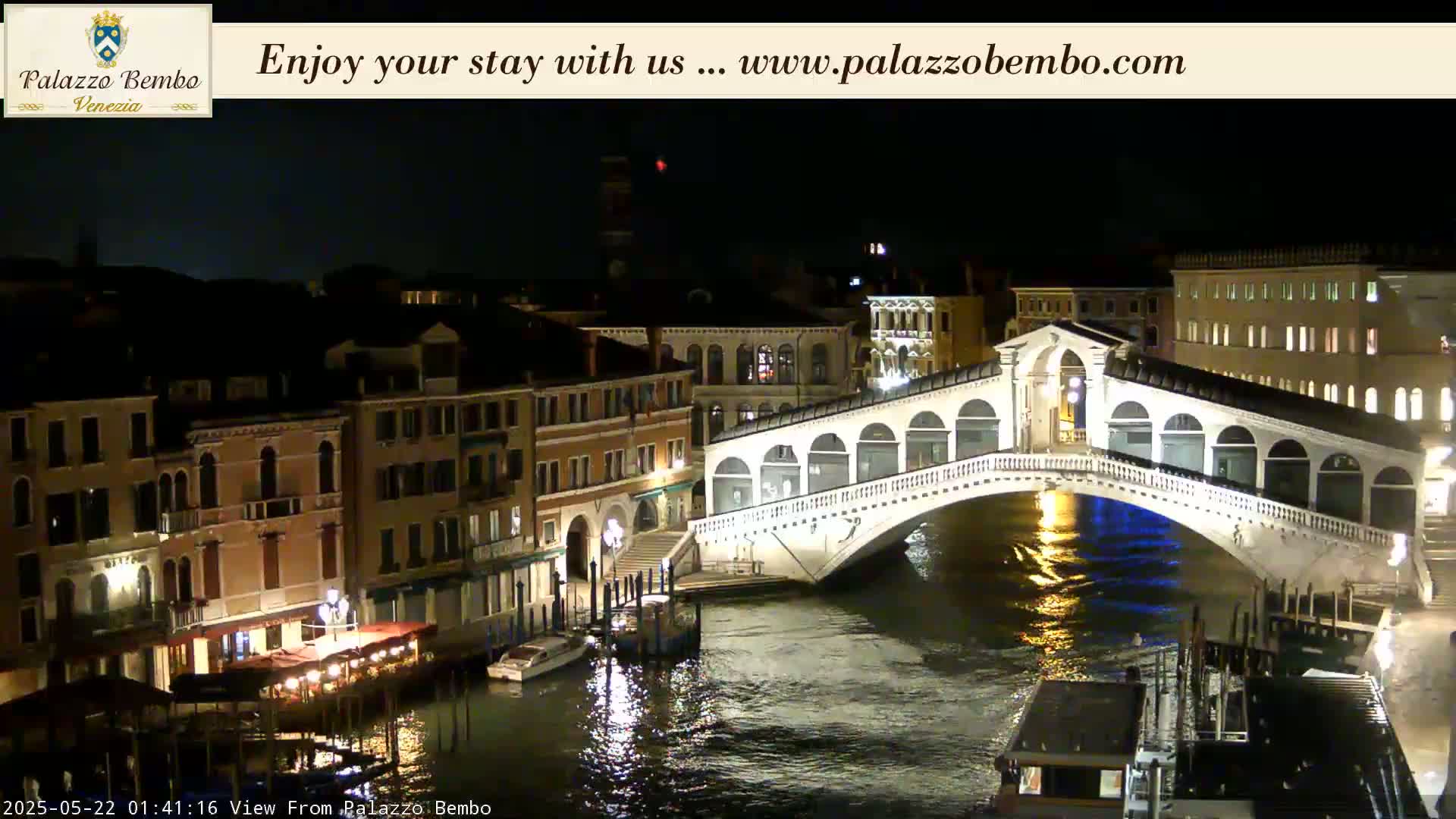 A nighttime view of a bridge over a canal in Venice, with illuminated buildings lining the waterway.