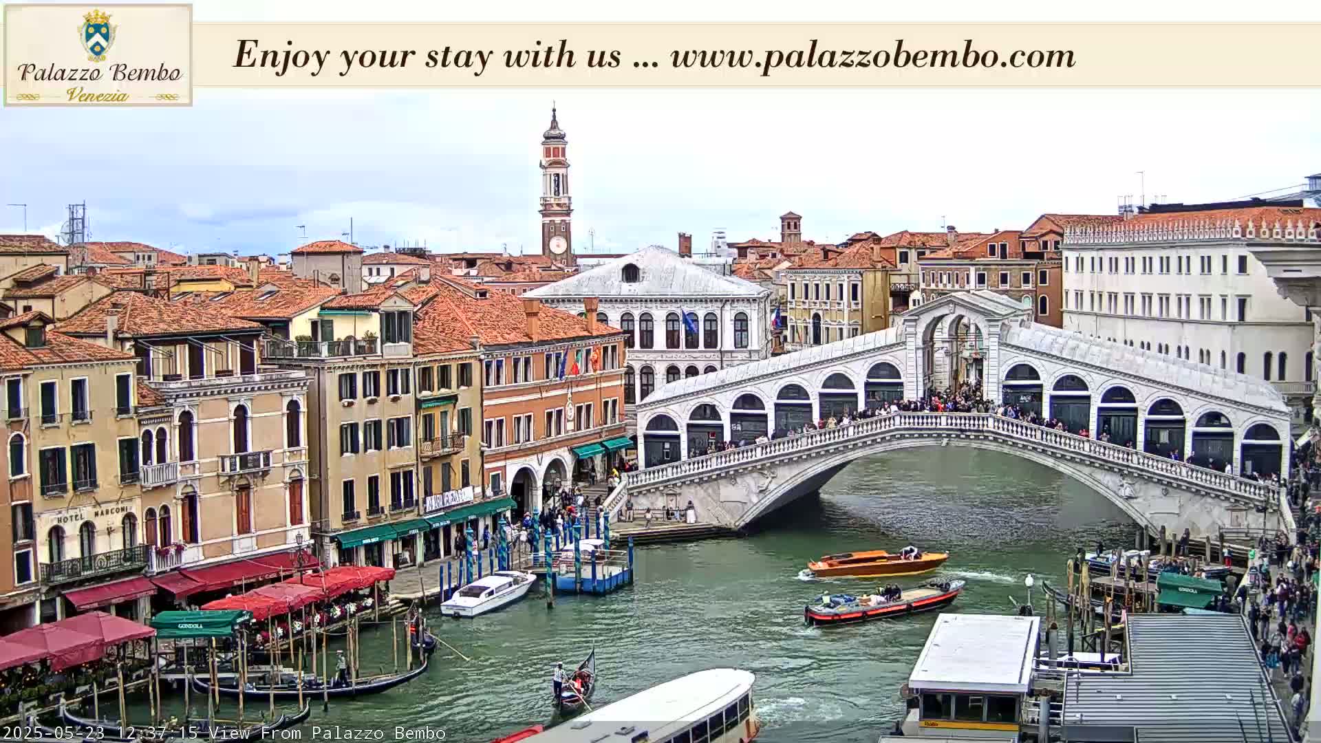 A view of the Rialto Bridge in Venice, Italy, on an overcast day, shows numerous boats in the canal below and pedestrians crossing the bridge.