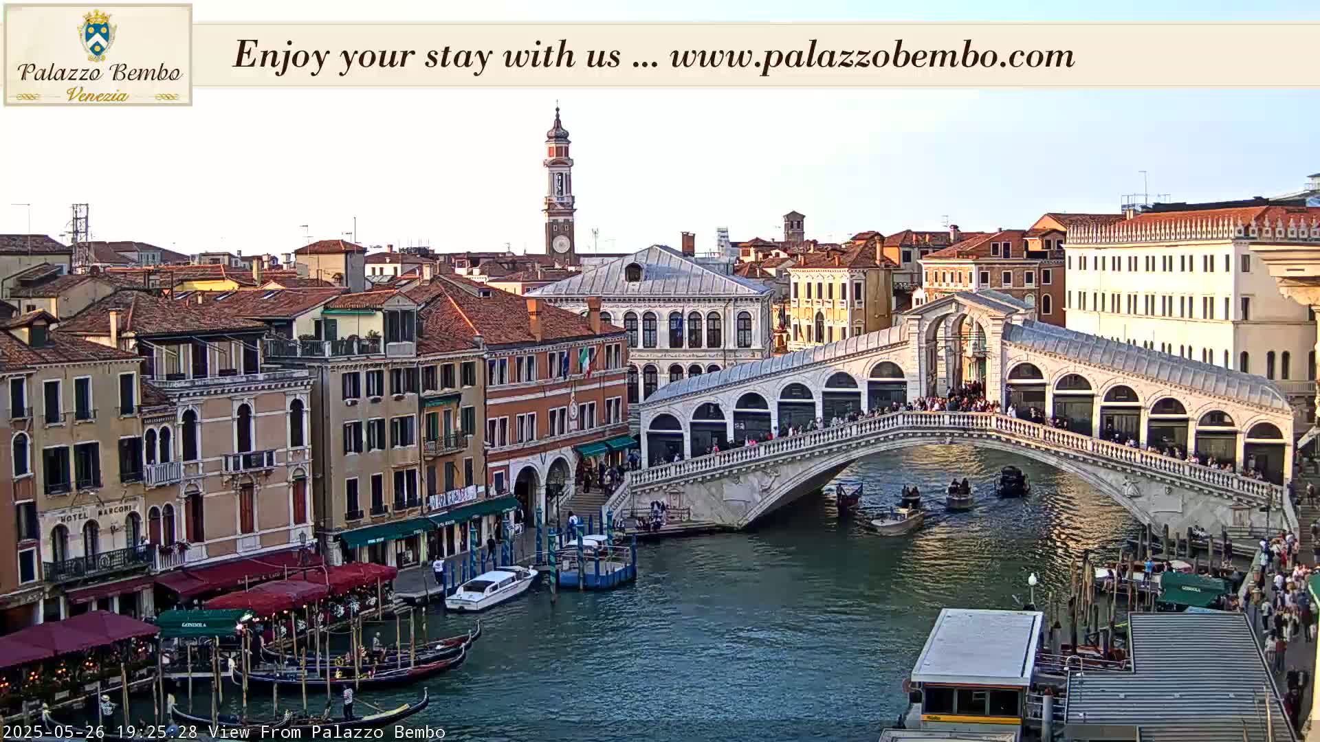 A Venetian canal scene at sunset shows a bridge crowded with people, gondolas in the water, and buildings lining the canal.