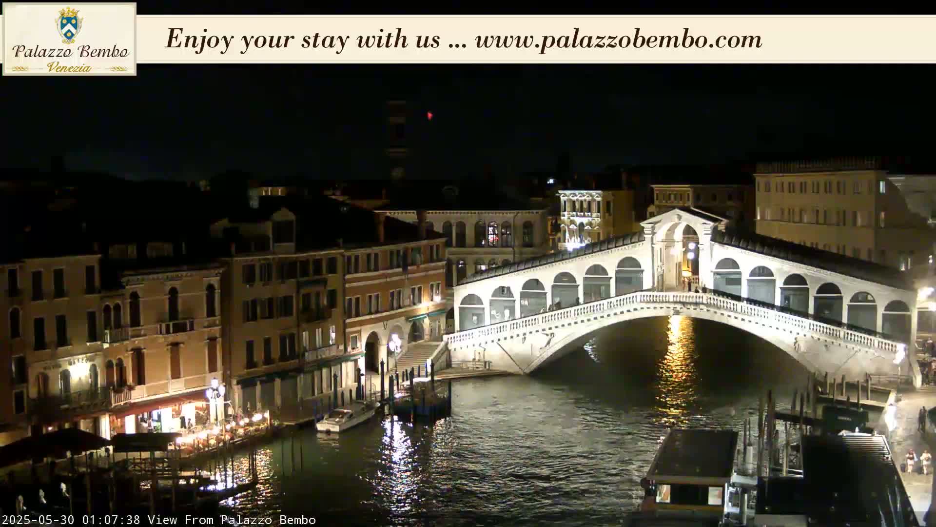 A nighttime view of a canal in Venice, showing a bridge illuminated against a dark sky.
