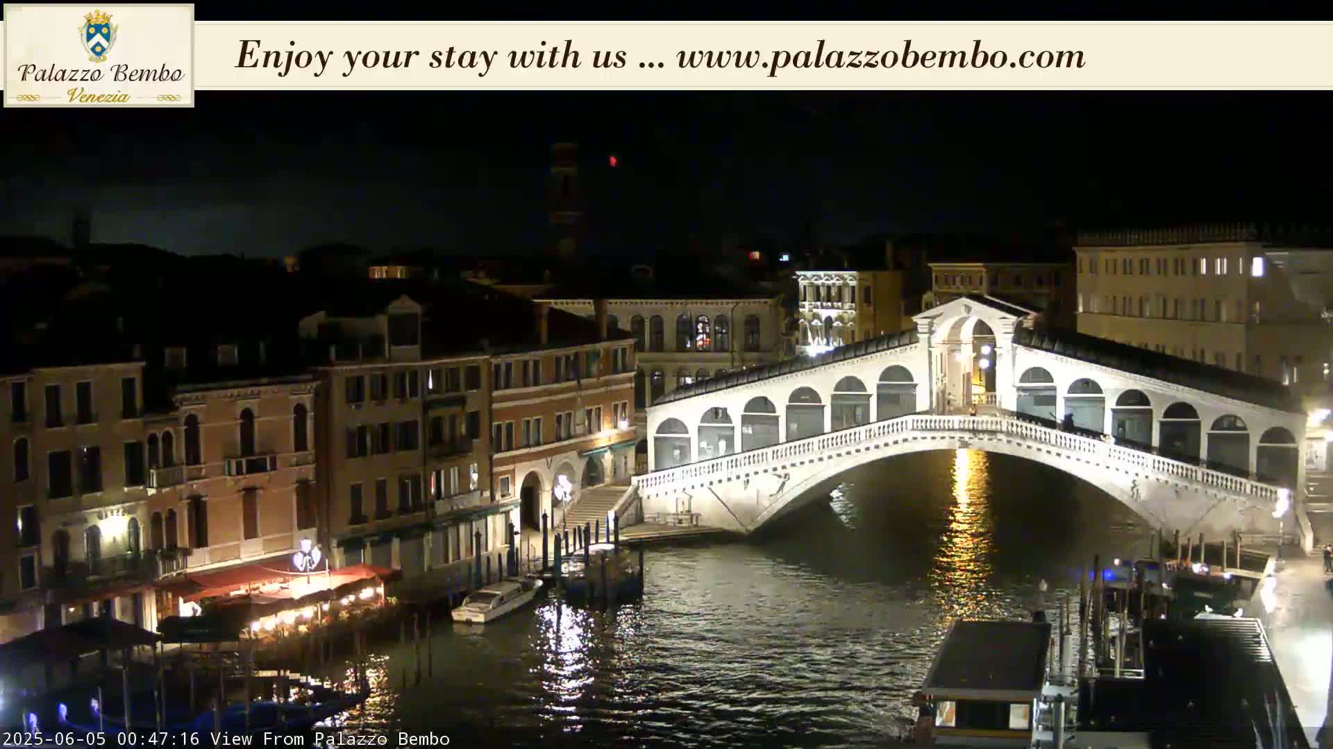 A nighttime view of a bridge over a canal in Venice, with buildings illuminated along the waterway.