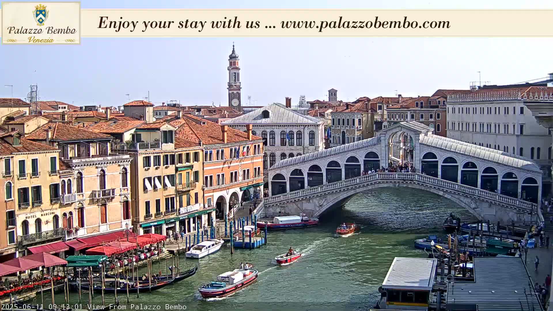 A sunny day in Venice shows a canal with boats, gondolas, and the Rialto Bridge lined with people, with colorful buildings along the waterway.