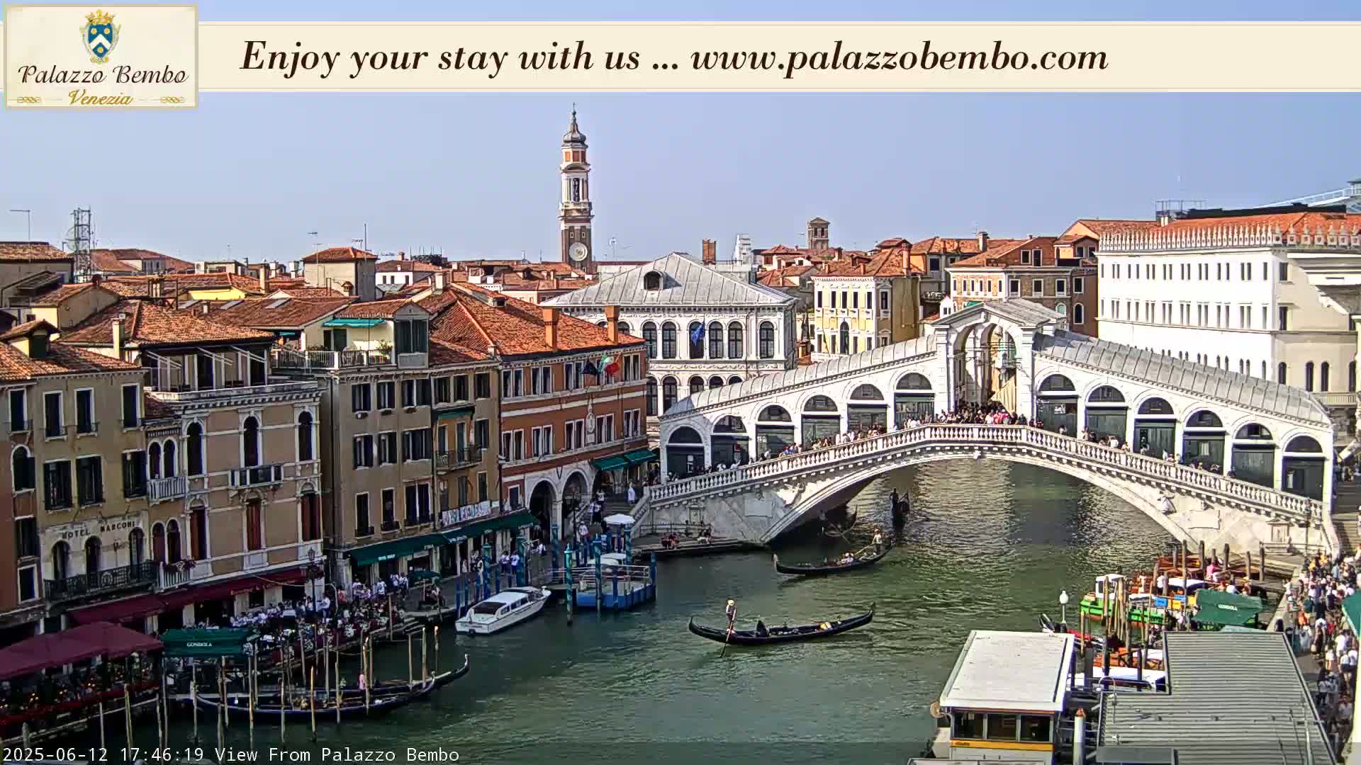 A sunny day in Venice shows a canal with gondolas and a footbridge crowded with people, surrounded by buildings with orange-red roofs.