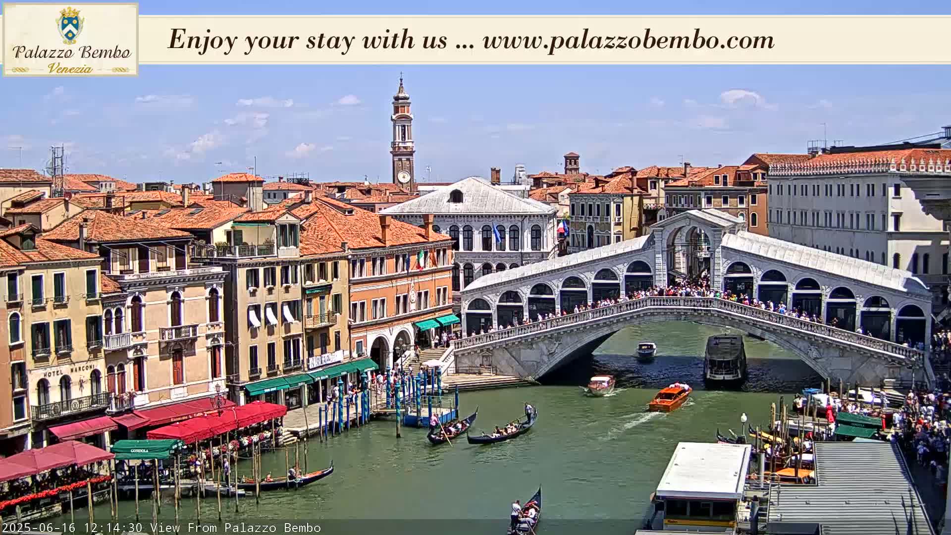 A sunny day in Venice shows the Rialto Bridge crowded with people, gondolas on the canal below, and numerous buildings lining the waterway.