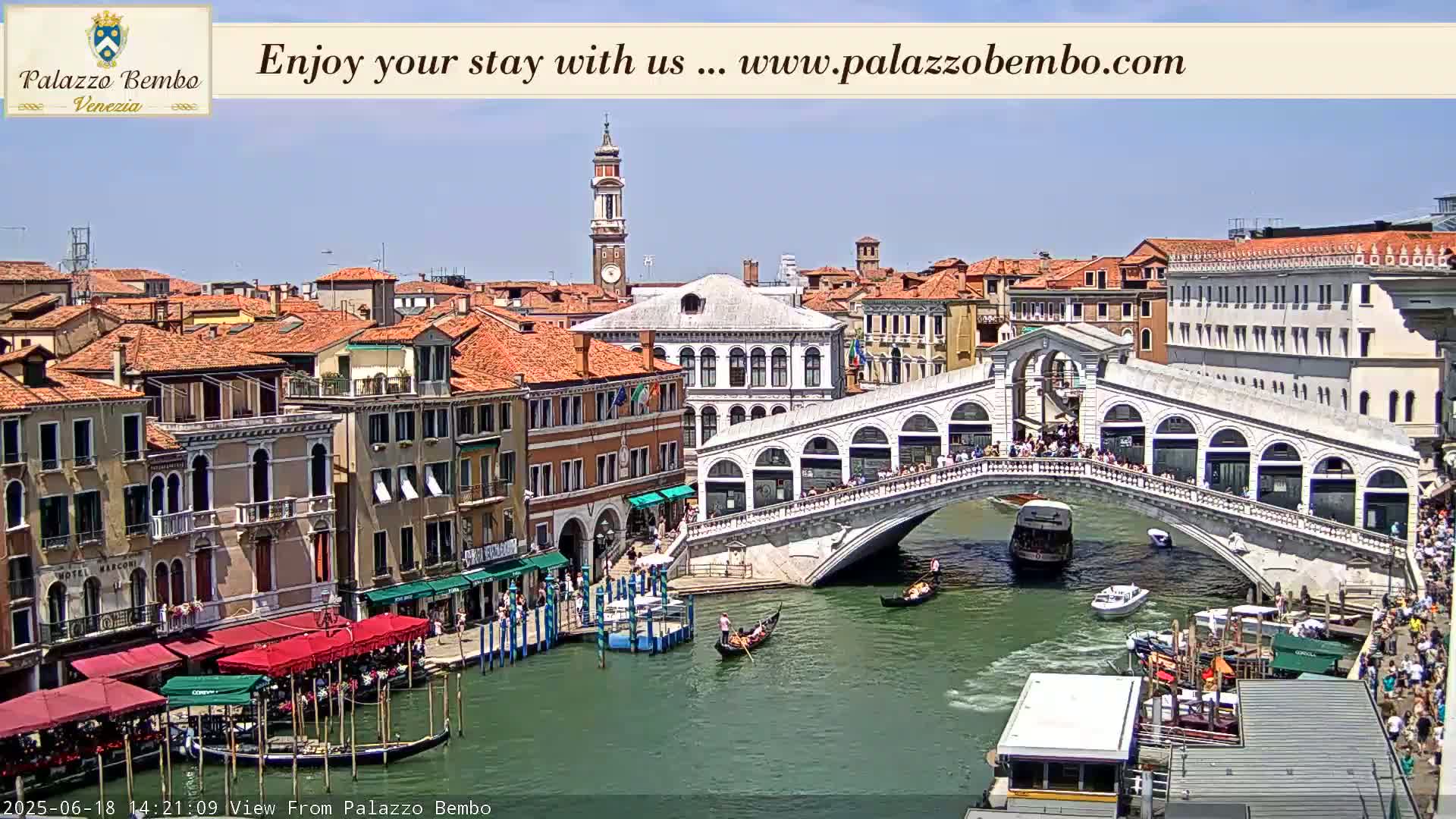 A sunny day in Venice shows a canal with gondolas and boats under the Rialto Bridge, lined with buildings.