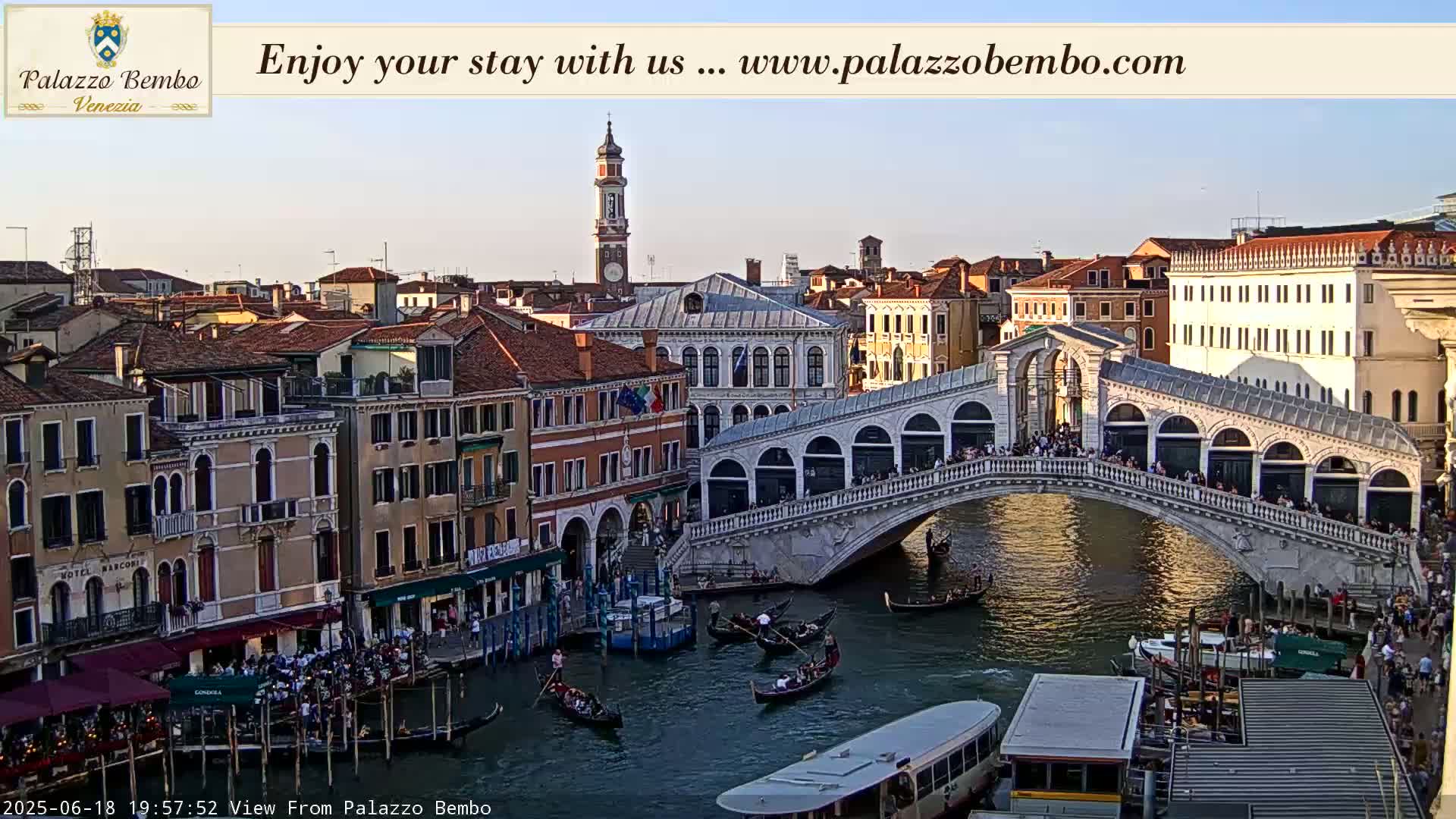 A Venetian bridge spans a canal filled with gondolas and boats under a clear, twilight sky.