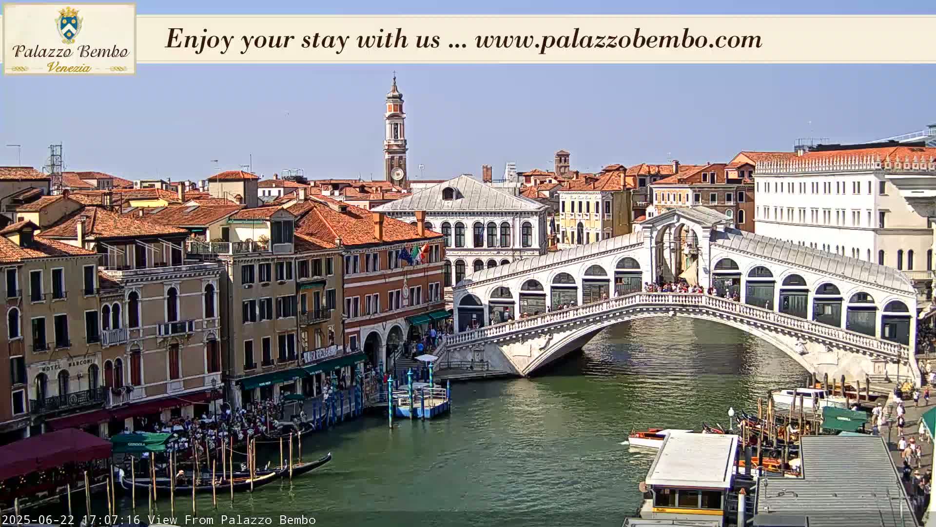 A sunny day in Venice shows a canal with gondolas, a bridge, and numerous buildings along the waterway.