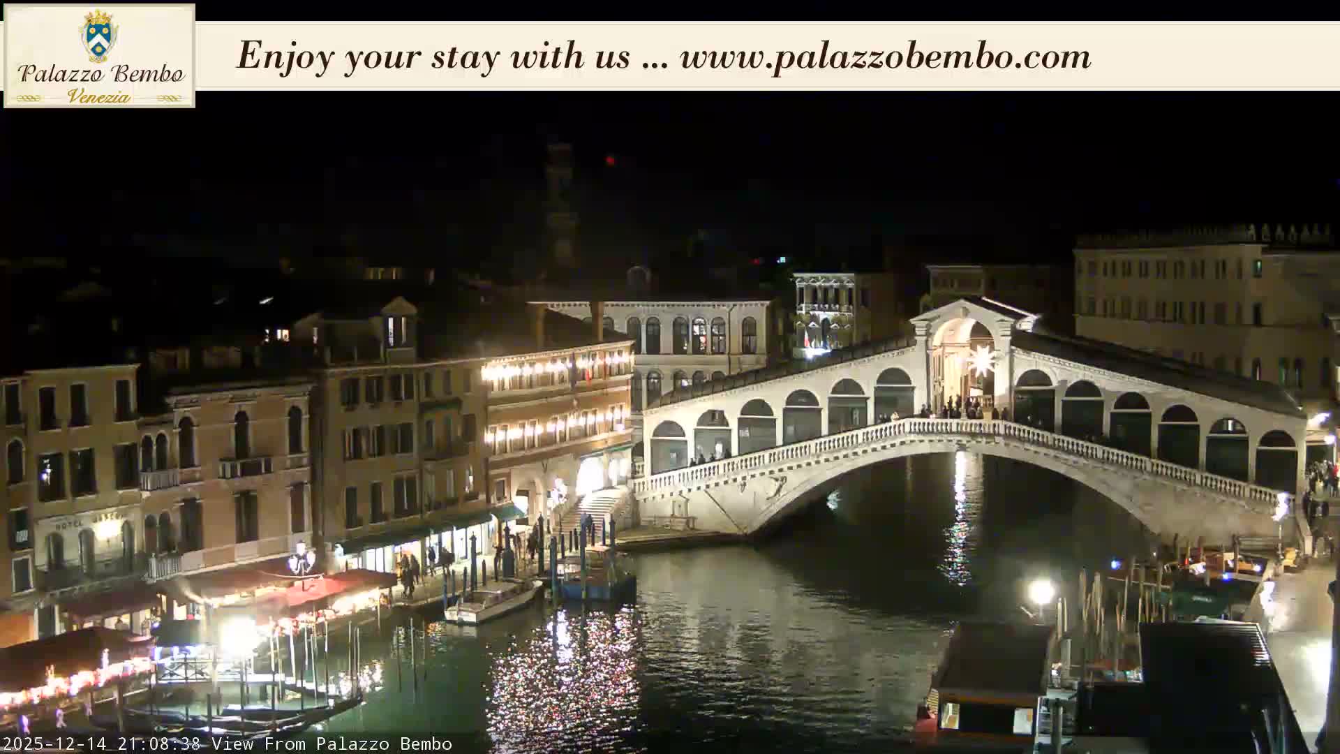 The iconic Rialto Bridge spans the Grand Canal in Venice, flanked by historic buildings and bustling with gondolas and various boats under a partly cloudy sky.