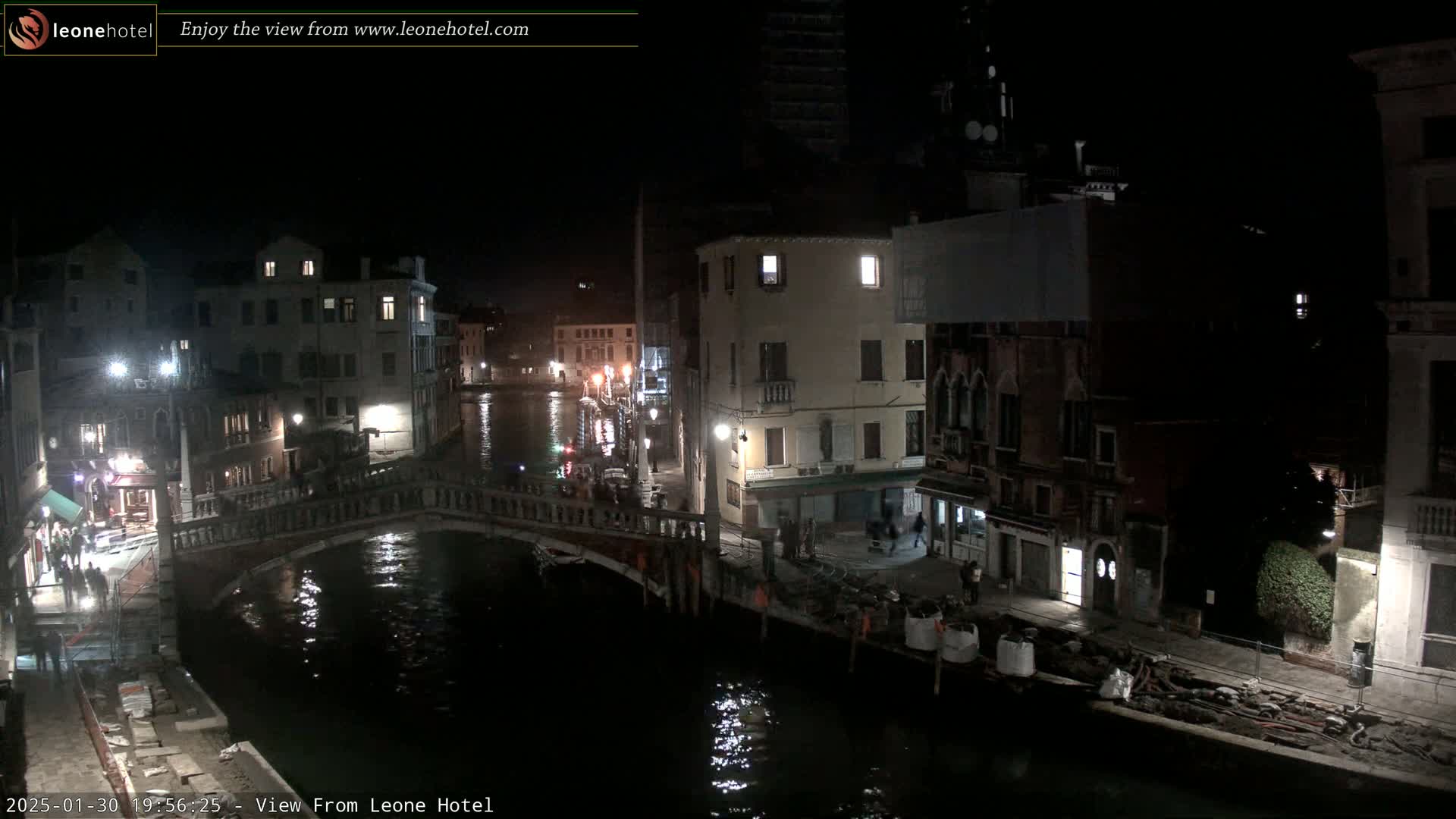 A nighttime view of a canal in Venice, showing buildings along the waterway and a bridge spanning the canal, with some construction visible near the water.