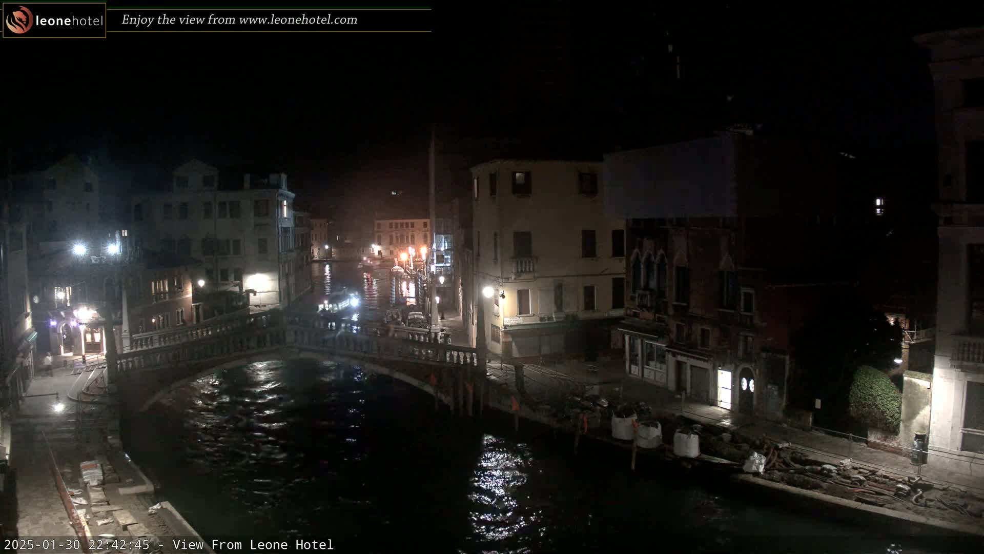 A nighttime view of a canal in Venice, showing several buildings along the waterway and a bridge crossing the canal.