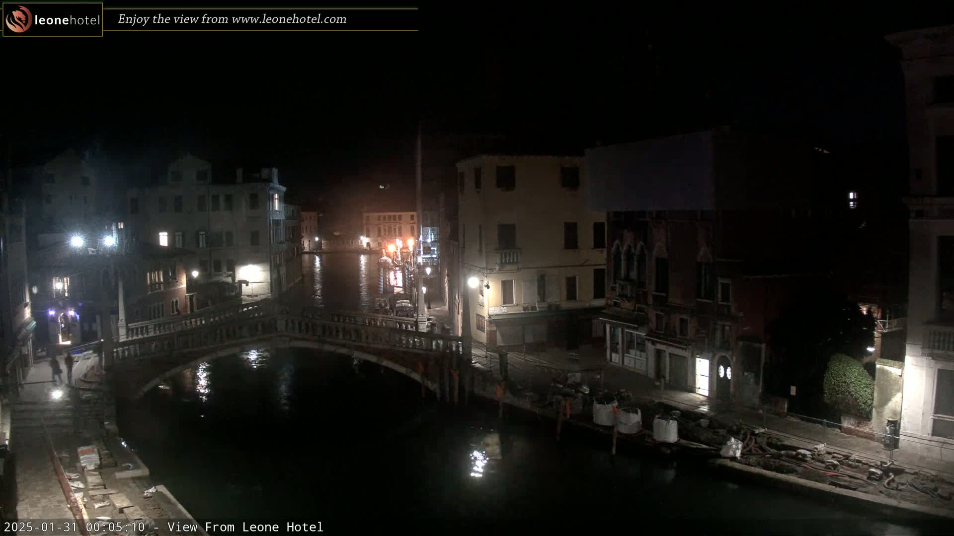 A nighttime view of a canal in Venice, Italy, shows a bridge, buildings along the waterway, and some construction materials on the bank.