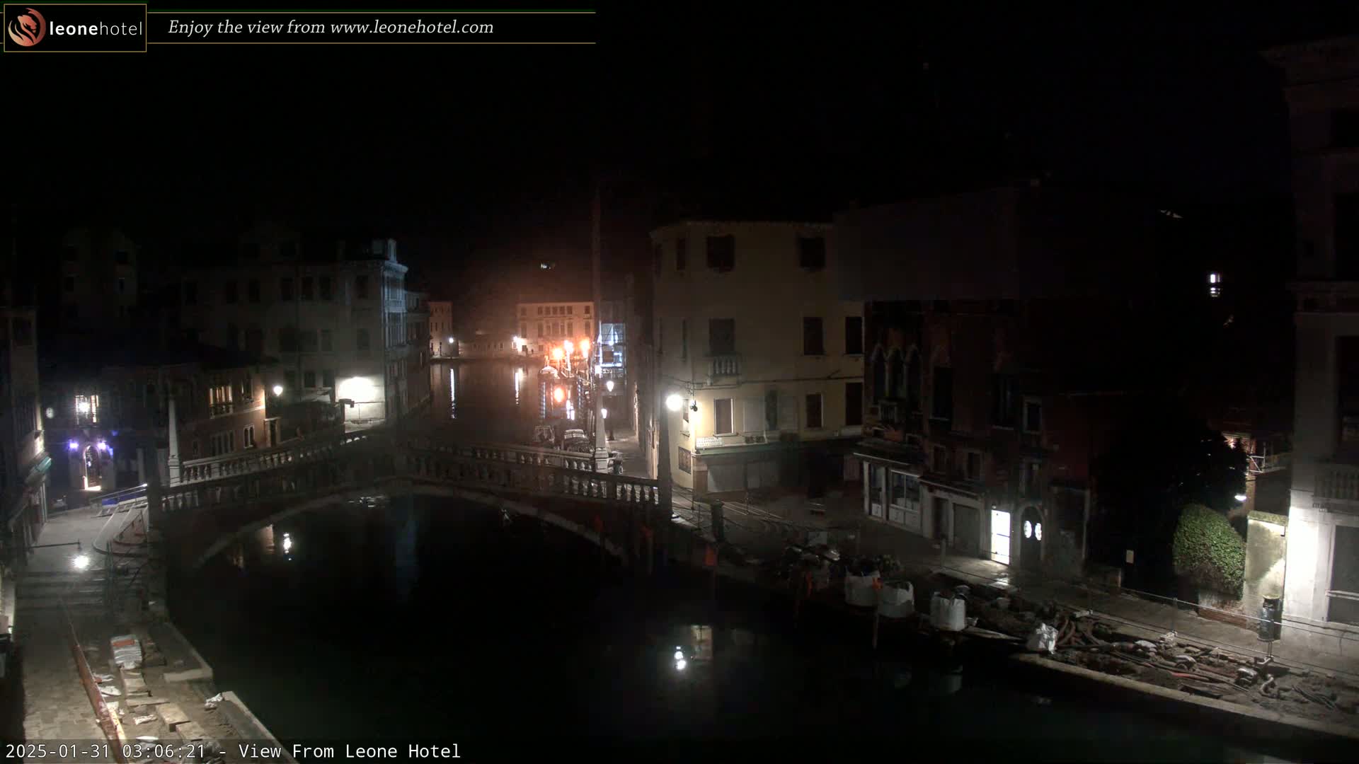 A nighttime view of a canal in Venice, Italy, shows a bridge and buildings along the waterway under dark, clear skies.