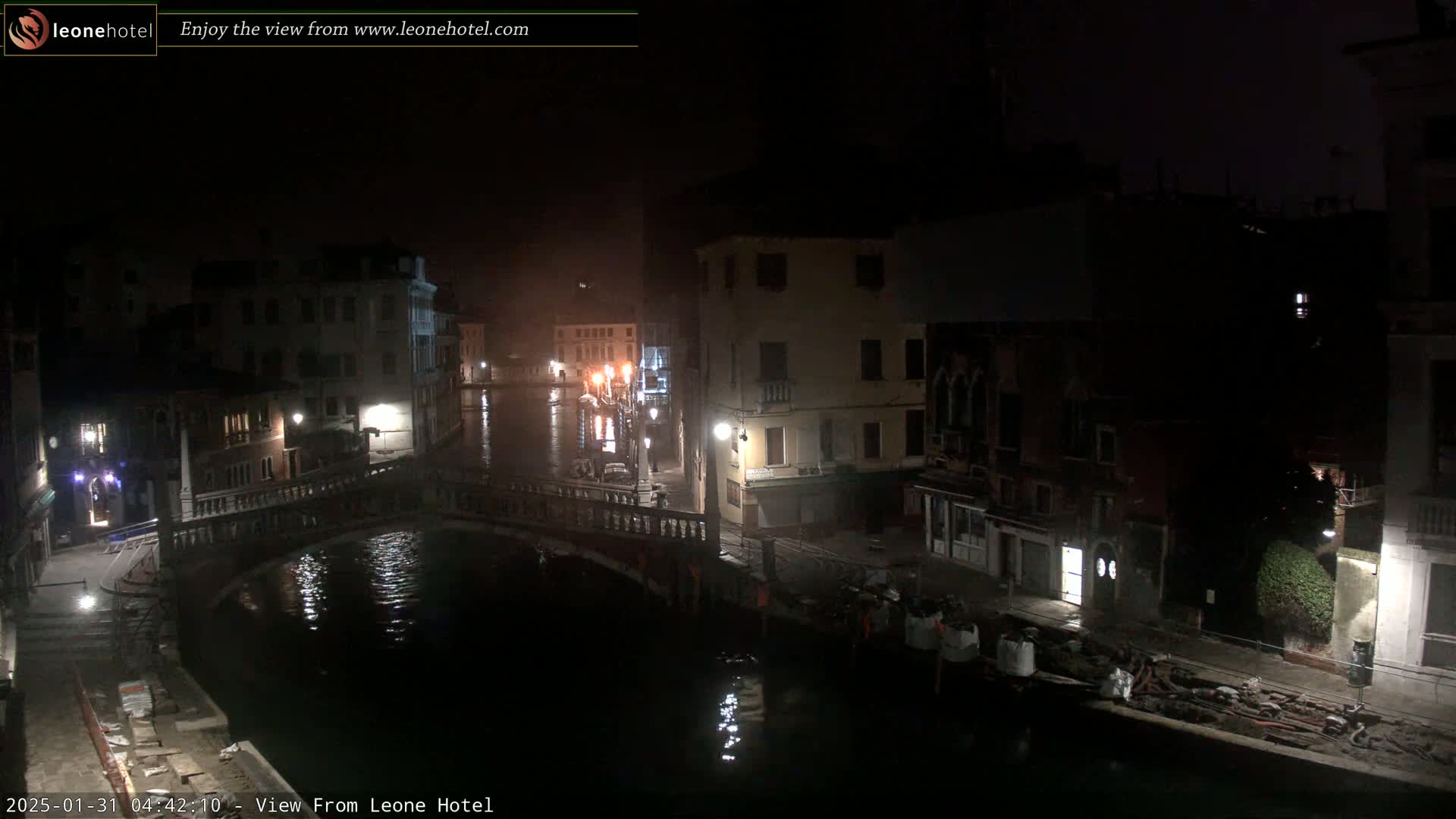 A nighttime view of a canal in Venice, showing bridges, buildings, and calm water.