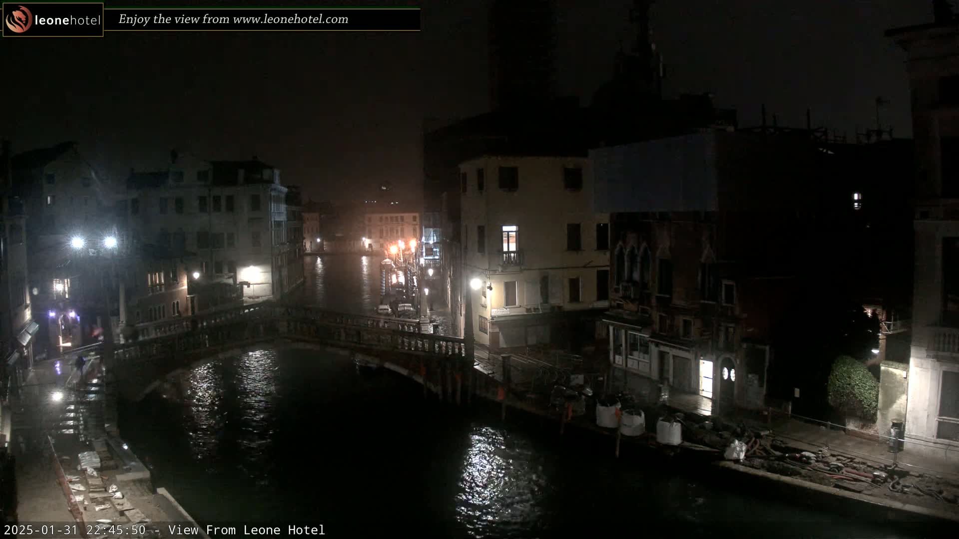 A nighttime view of a canal in Venice, with rain falling on buildings and a bridge.