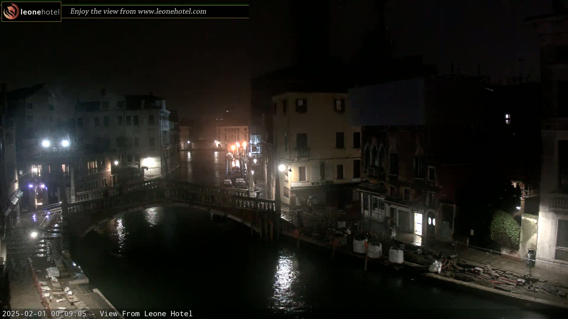 A nighttime view of a canal in Venice, Italy, showing buildings lining the waterway and a bridge crossing it under rainy conditions.