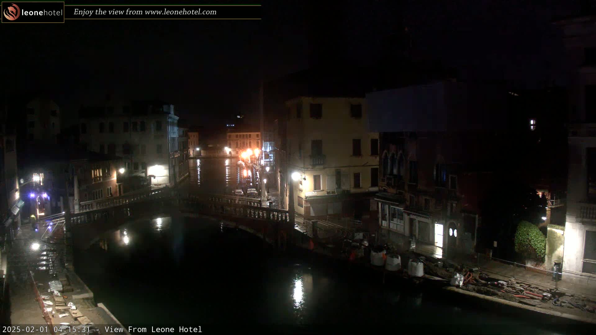 A nighttime view of a canal in Venice, Italy, showing buildings lining the waterway, a bridge, and some construction materials on the banks.