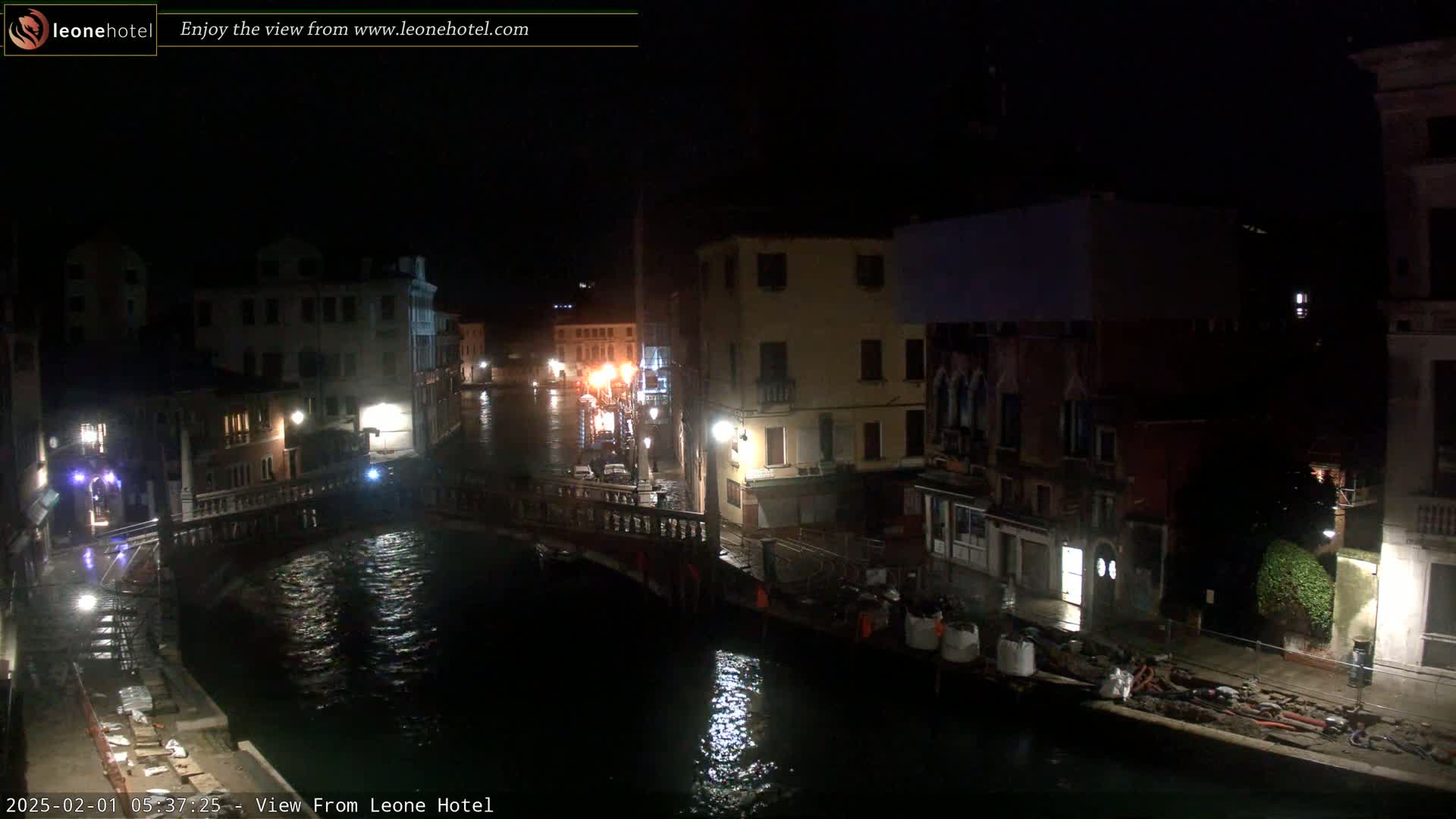 A nighttime view of a canal in Venice, with buildings lining the waterway, a bridge spanning the canal, and some construction materials visible on the canal banks.
