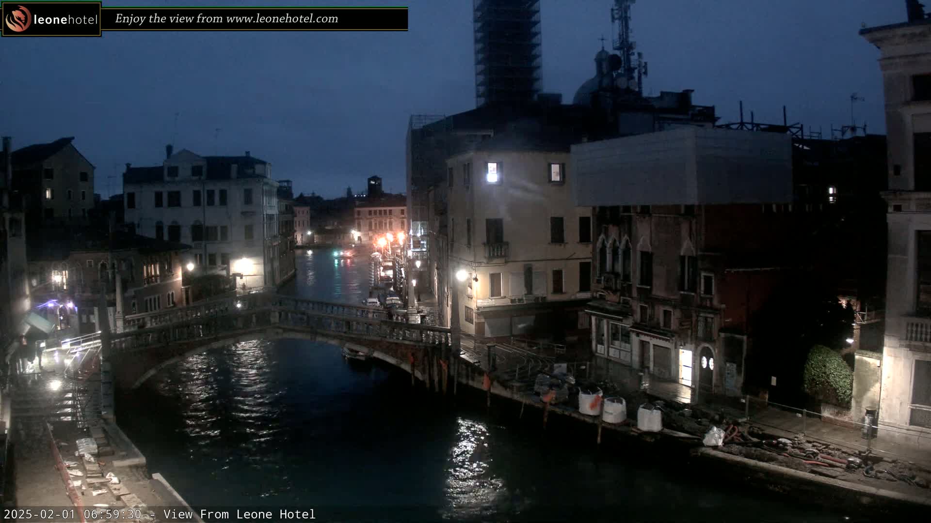 A nighttime view of a canal in Venice, Italy, shows several buildings lining the waterway, with a bridge crossing the canal, under a dark, overcast sky.
