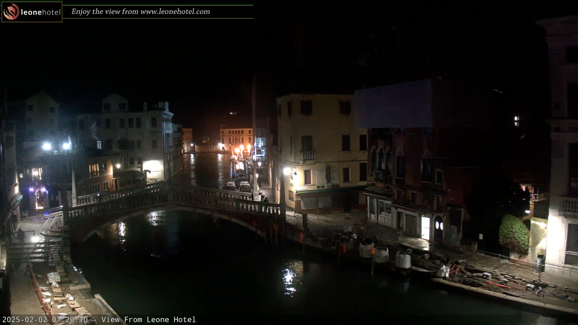 A nighttime view of a canal in Venice, Italy, showing several buildings along the waterway and a bridge spanning the canal, with construction materials visible near the water's edge.
