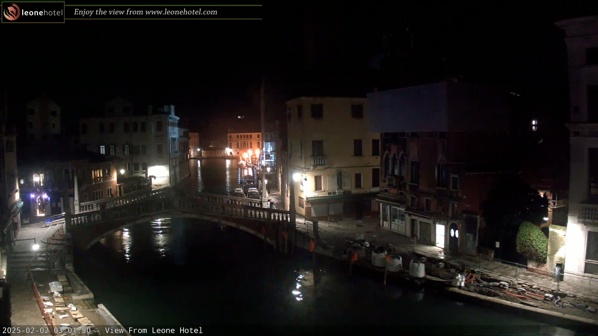 A nighttime view of a canal in Venice, Italy, showing a bridge, buildings, and calm water.