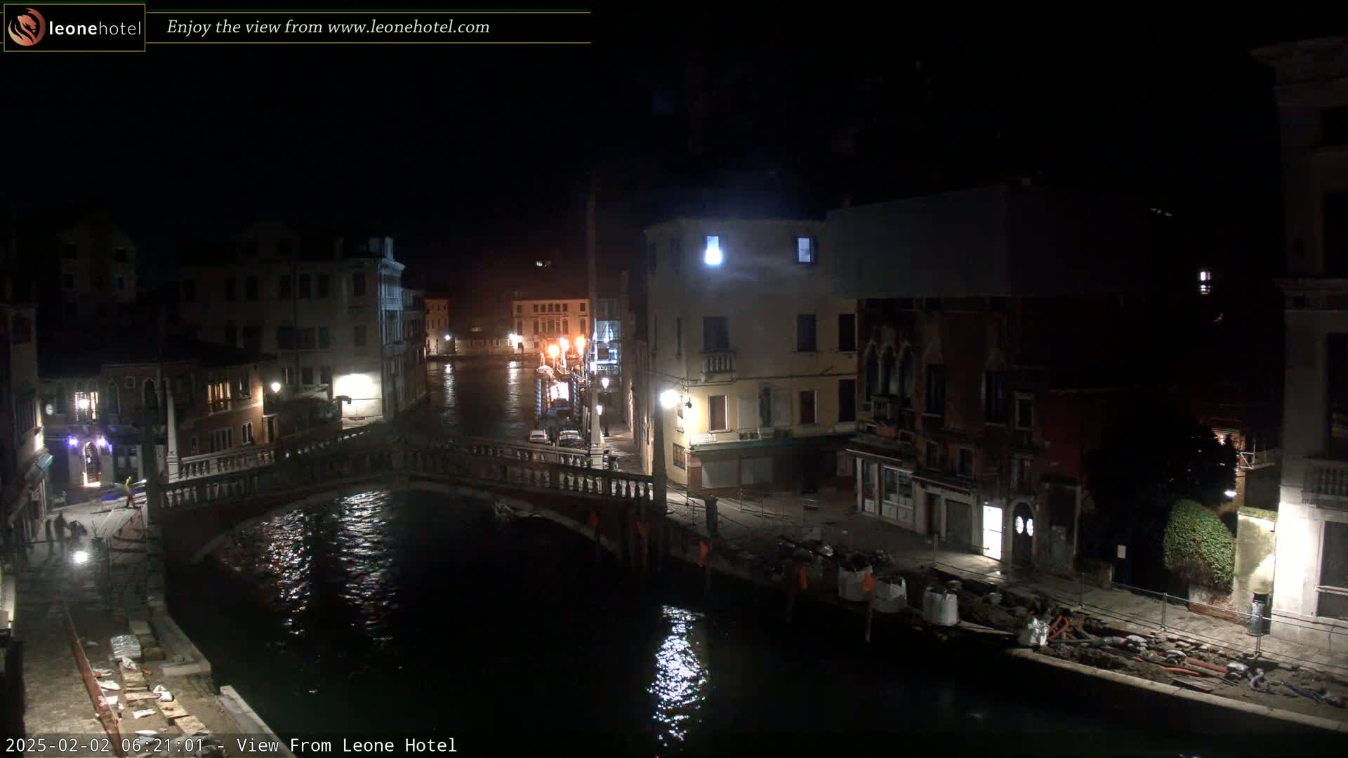 A nighttime view of a canal in Venice, Italy, shows a bridge, several buildings, and some construction along the waterway.