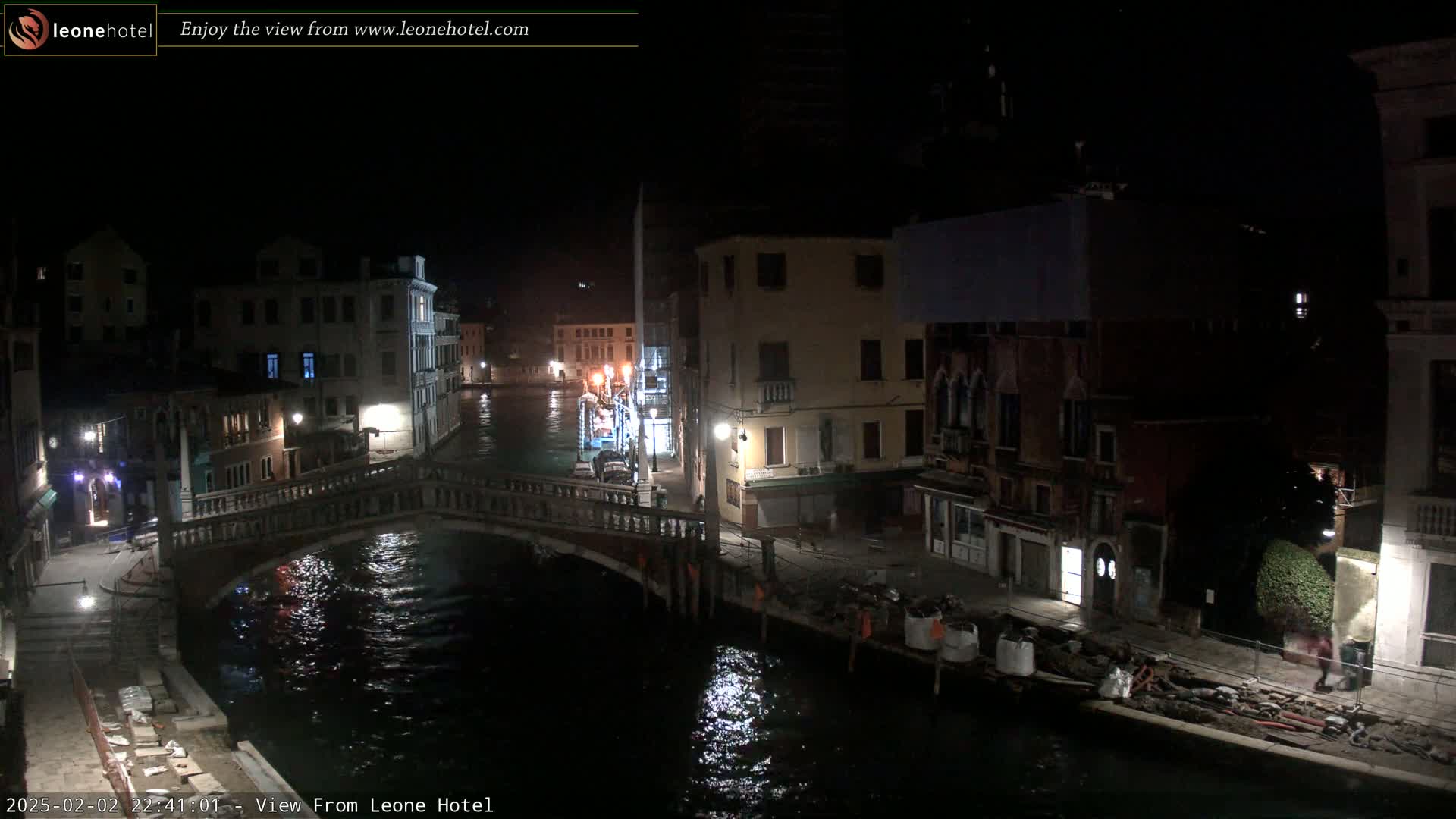 A nighttime view of a canal in Venice, Italy, shows a bridge and several buildings along the waterway, under a clear, dark sky.