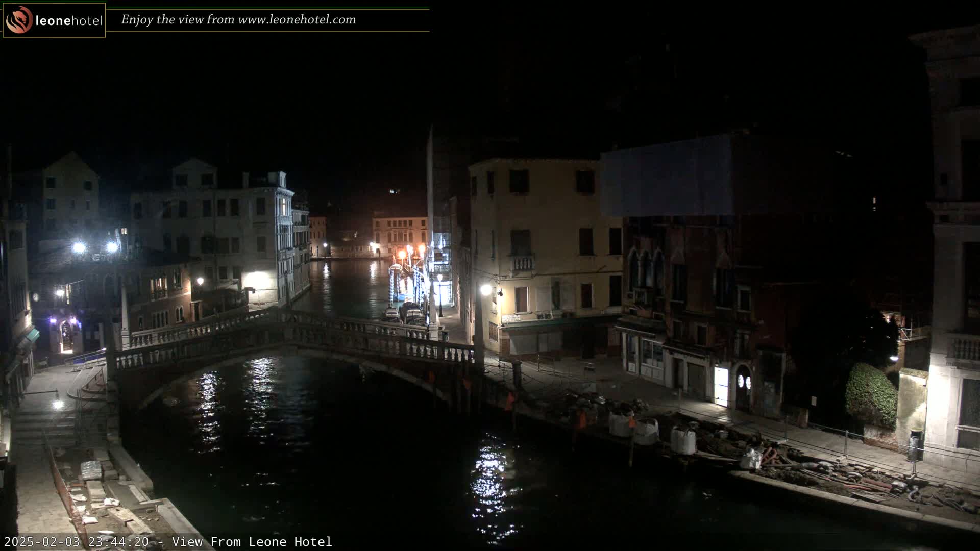 A nighttime view of a canal in Venice, Italy, with buildings lining the waterway and a bridge crossing the canal.