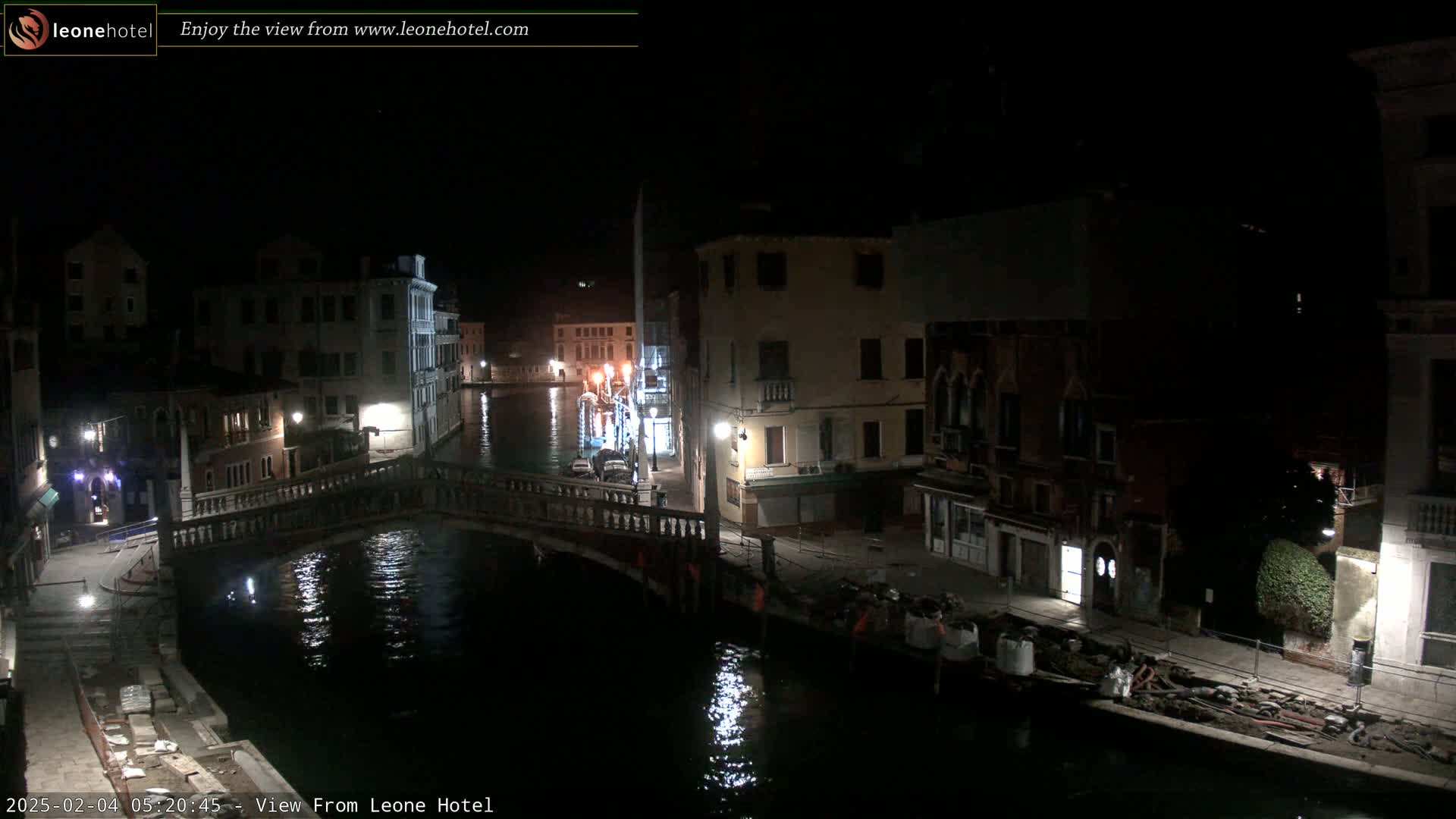 A nighttime view of a canal in Venice, showing a bridge, buildings lining the waterway, and some construction materials along the edge of the canal.