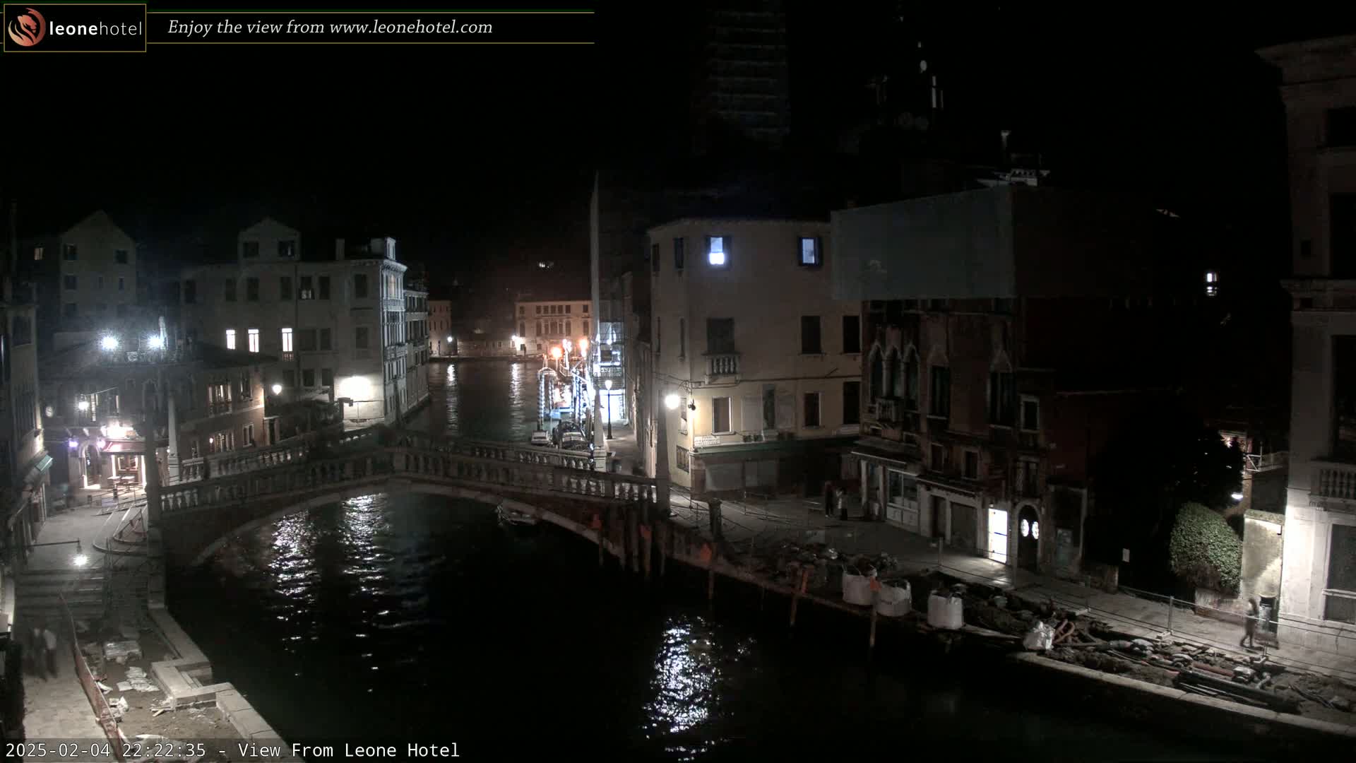 A nighttime view of a canal in Venice, Italy, showing bridges, buildings, and some construction activity along the water's edge.