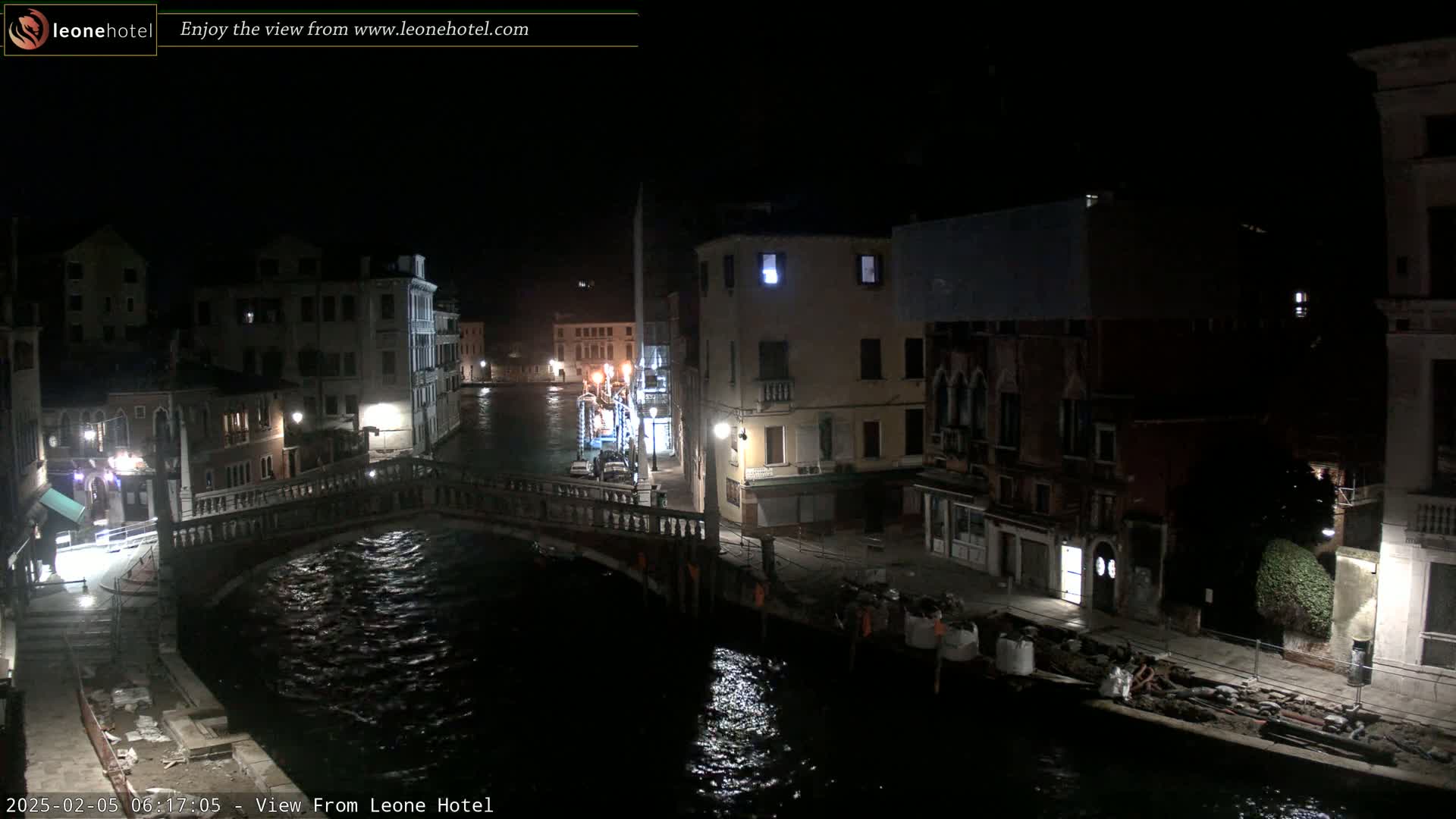 A nighttime view of a canal in Venice, showing a stone bridge, buildings lining the waterway, and calm water reflecting light.