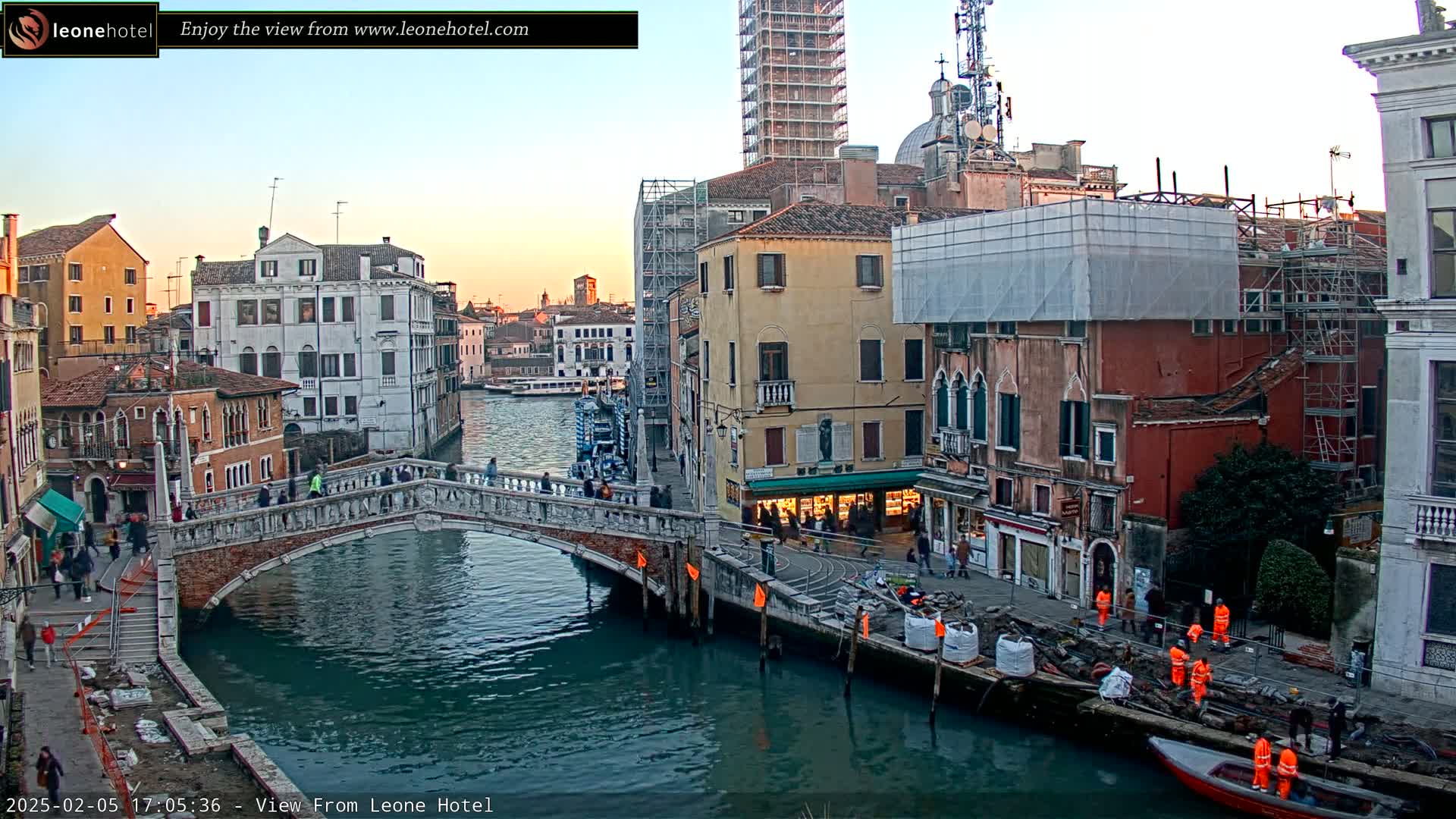 A stone bridge arches over a canal in Venice, Italy, with colorful buildings lining the waterway under a twilight sky.