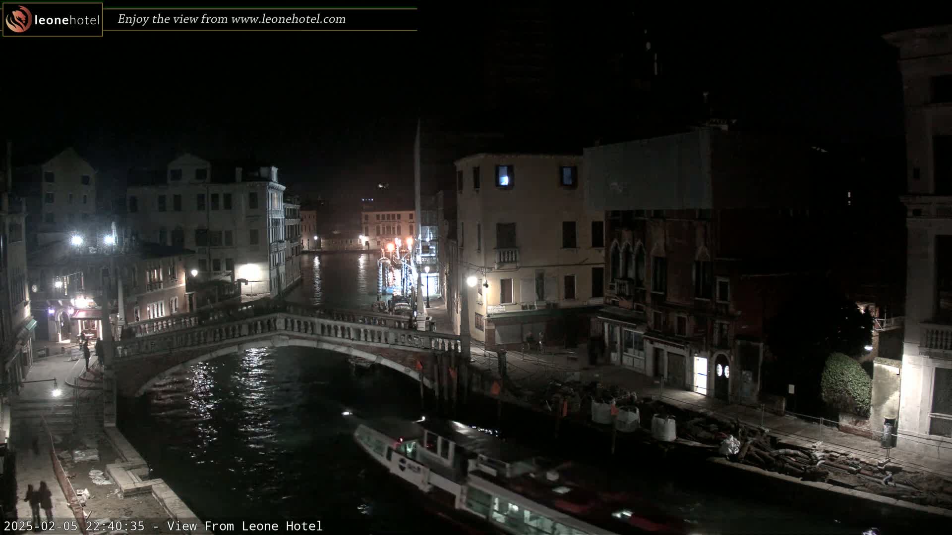 A nighttime view of a canal in Venice, showing bridges, buildings, and a boat on the water.