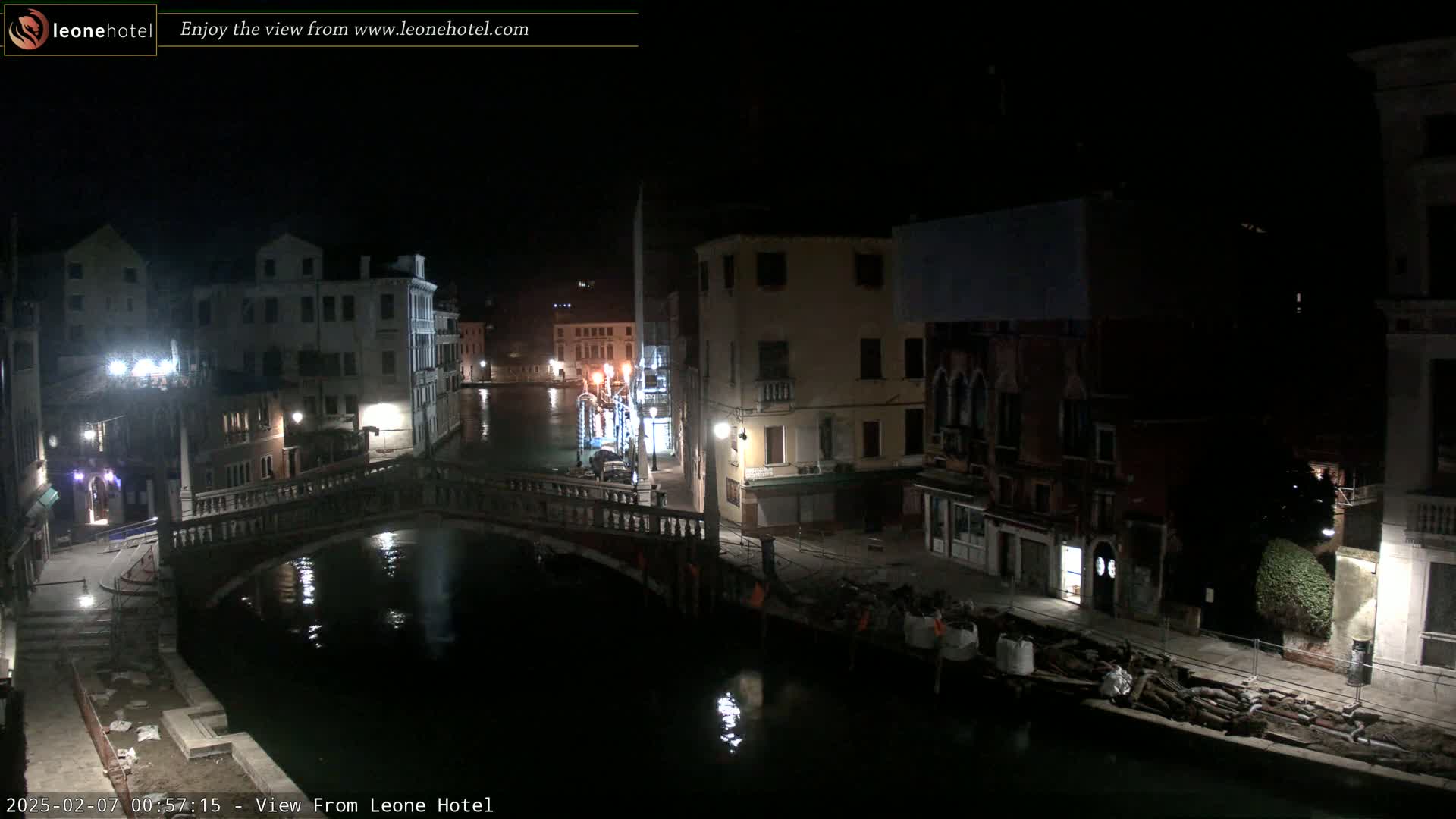 A nighttime view of a canal in Venice, Italy, shows a bridge, buildings along the water's edge, and some construction materials on the canal bank.