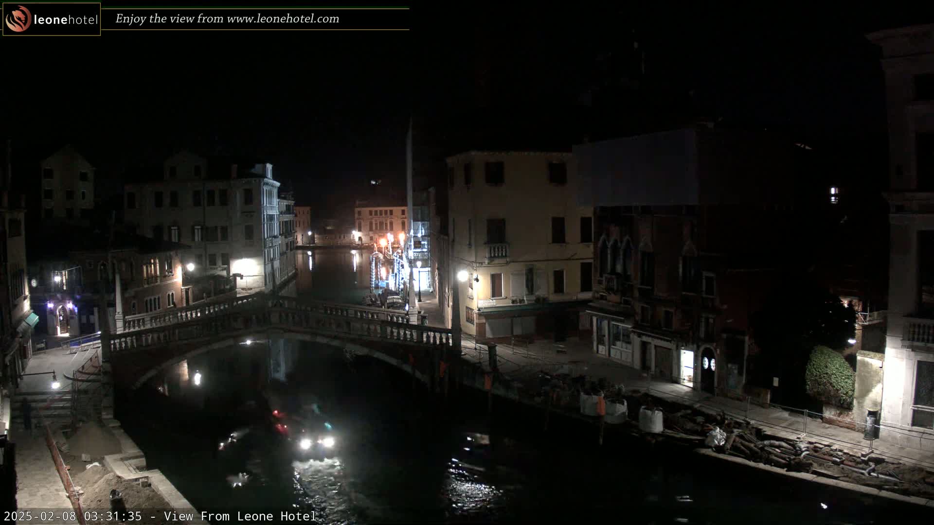 A nighttime view of a canal in Venice, with a bridge, buildings, and boats visible under dark, clear skies.