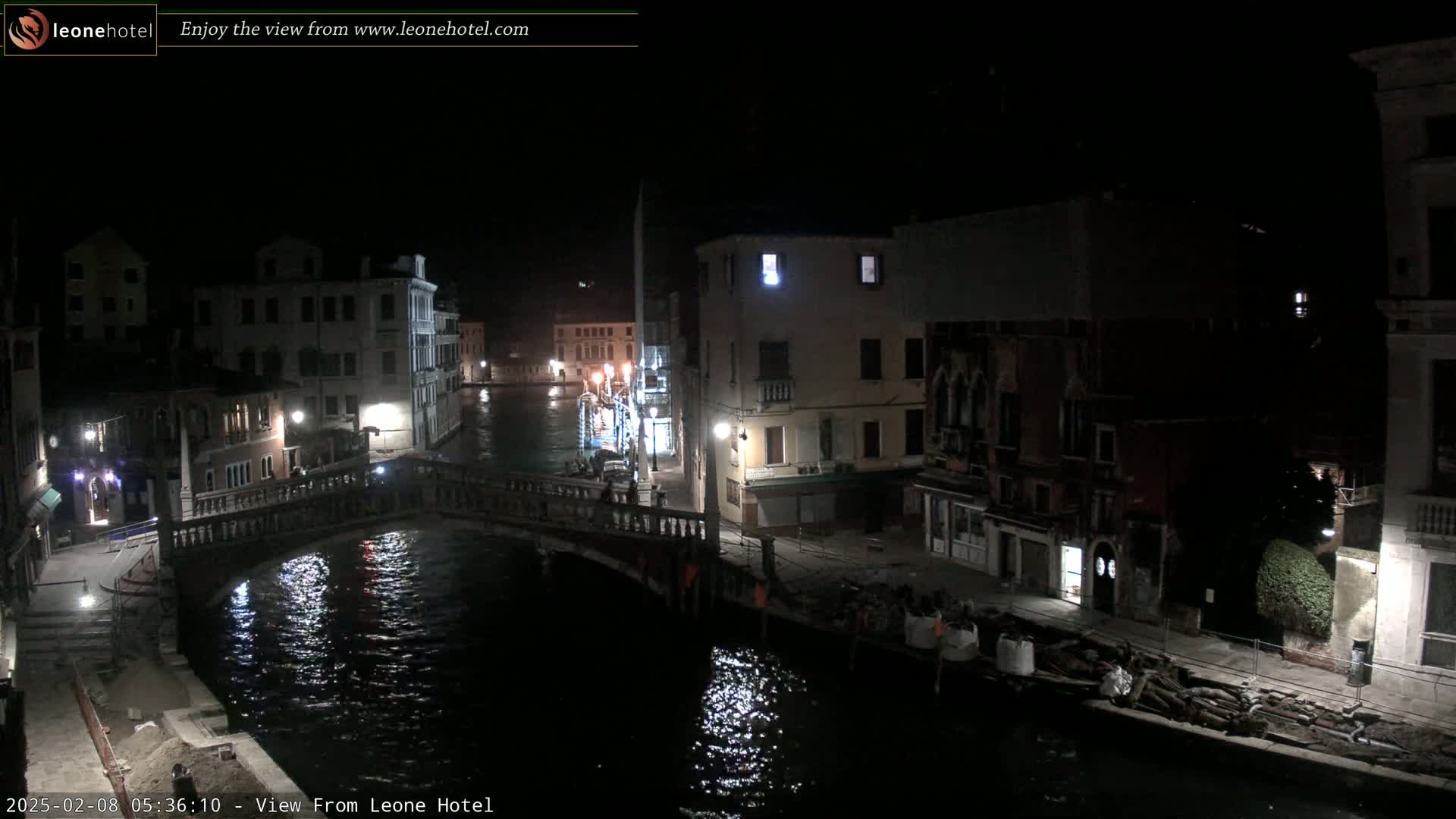 A nighttime view of a canal in Venice, showing a bridge and buildings along its banks under a dark sky.