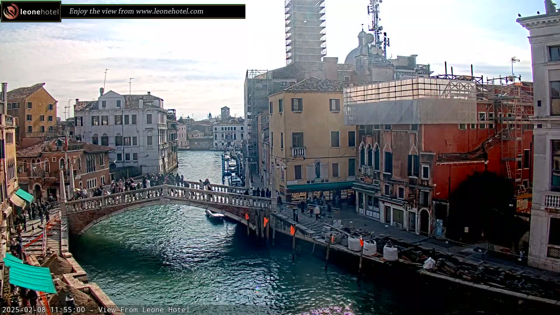 A bridge over a canal in Venice, Italy, is filled with people under a cloudy sky.
