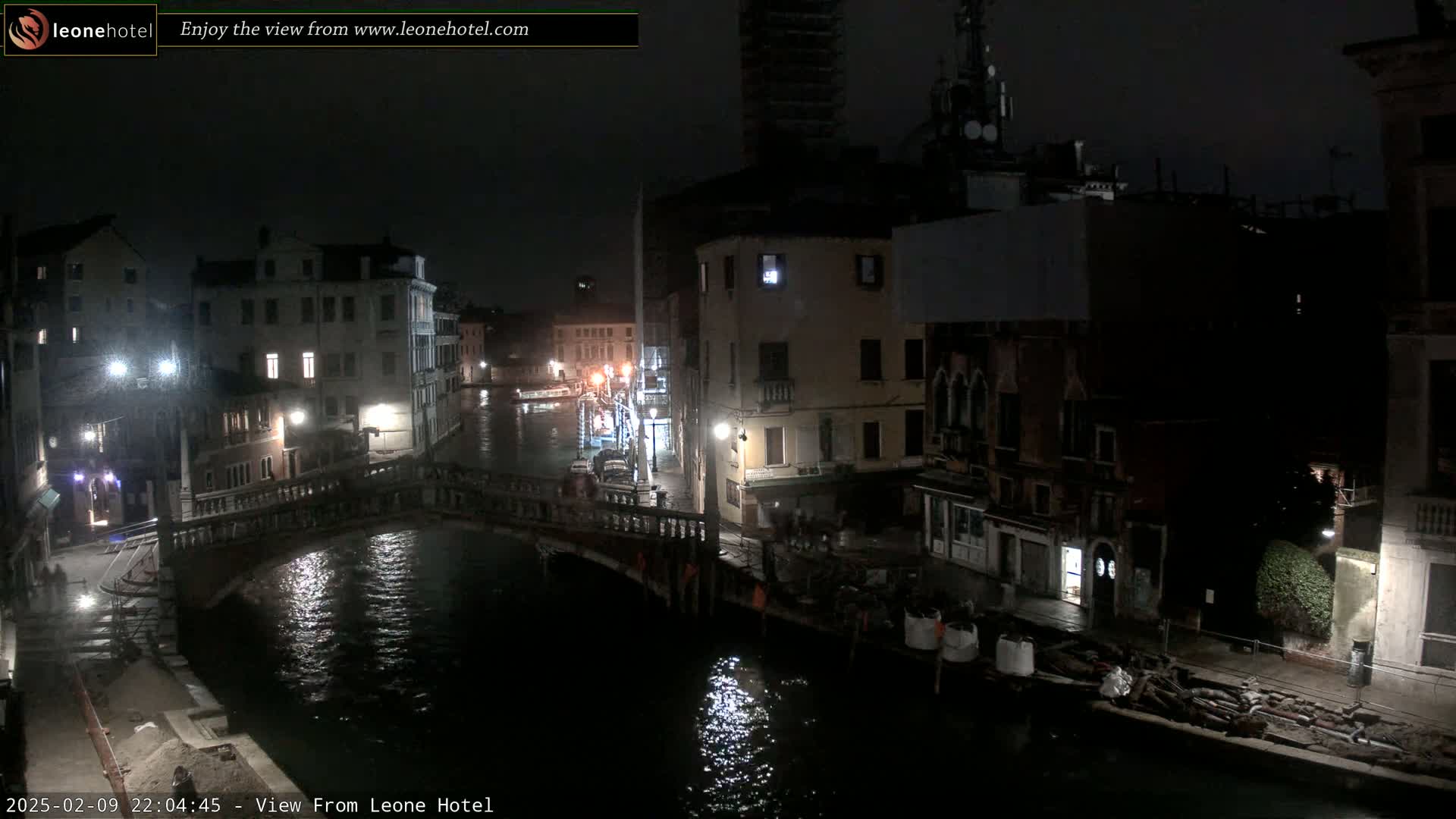 A nighttime view of a canal in Venice, Italy, shows a bridge and several buildings under a dark, possibly rainy sky.