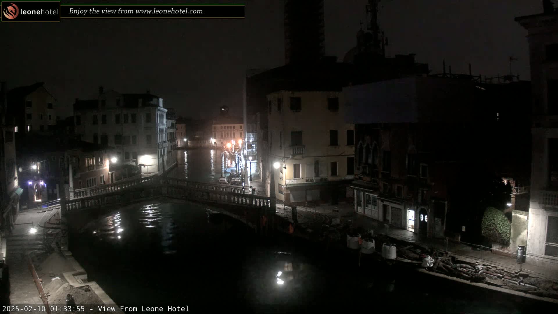 A nighttime view of a canal in Venice, Italy, shows several buildings along the waterway and a bridge crossing the dark water.