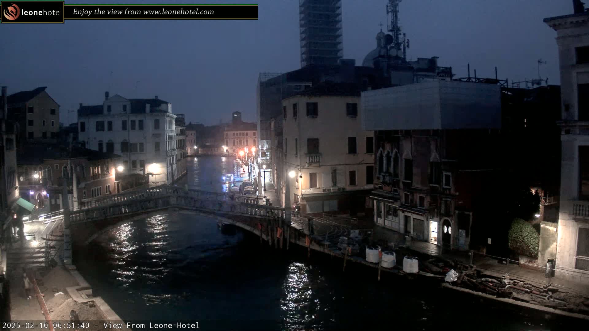 A nighttime view of a canal in Venice, Italy, shows several buildings along the waterway and a bridge crossing the canal under a dark, overcast sky.