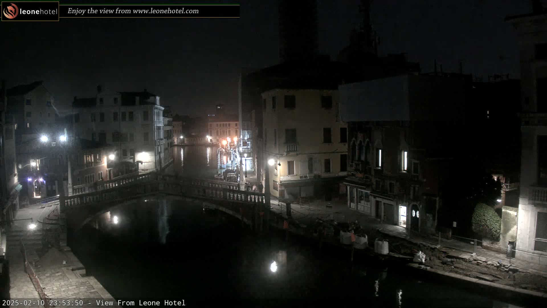 A nighttime view of a canal in Venice, Italy, shows several buildings along the waterway, a bridge, and calm water reflecting the lights.
