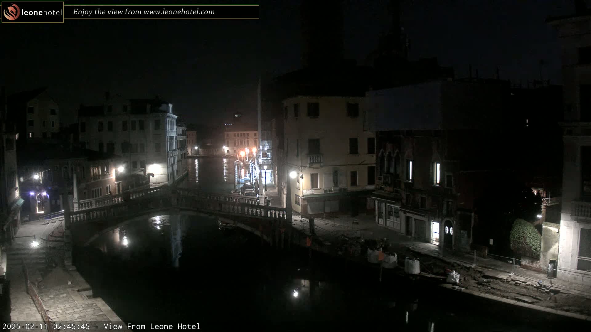 A nighttime view of a canal in Venice, Italy, with buildings lining the waterway and a bridge visible.
