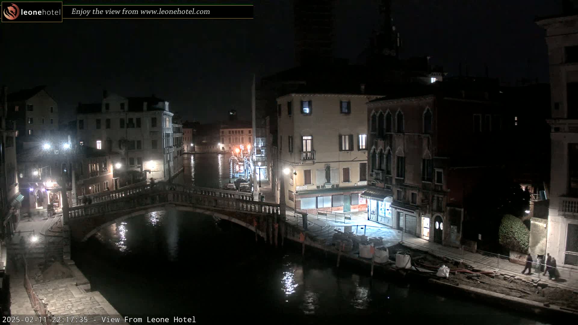 A nighttime view of a canal in Venice, Italy, shows a bridge, buildings along the waterway, and calm water reflecting the lights.