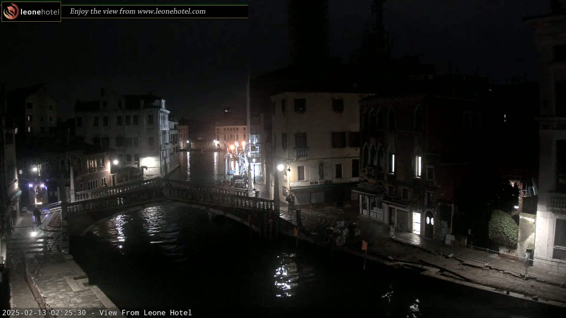 A nighttime view of a canal in Venice, showing several buildings and a bridge, under a clear, dark sky.