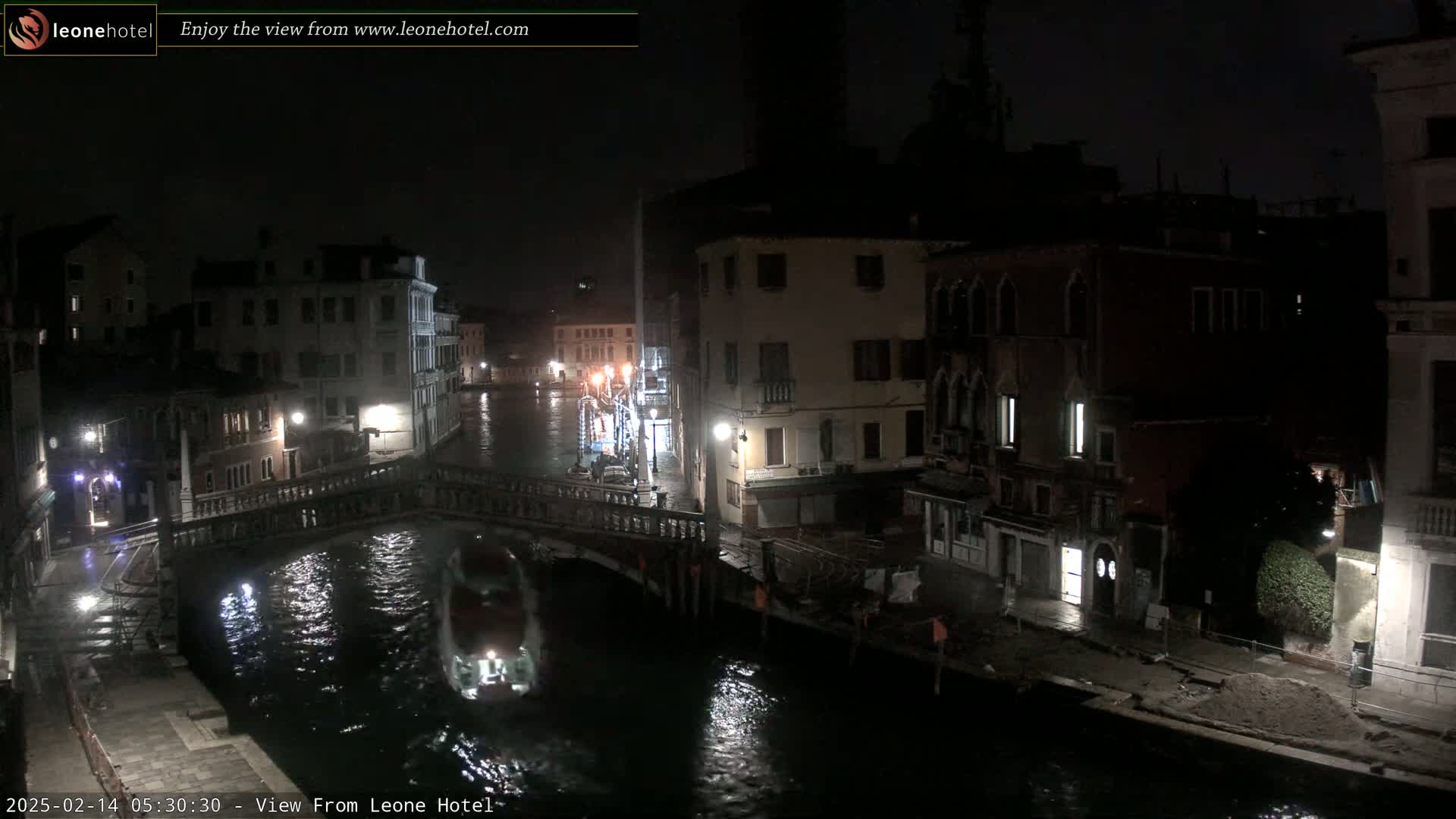 A nighttime view of a canal in Venice, with buildings lining the waterway and a boat passing under a bridge.