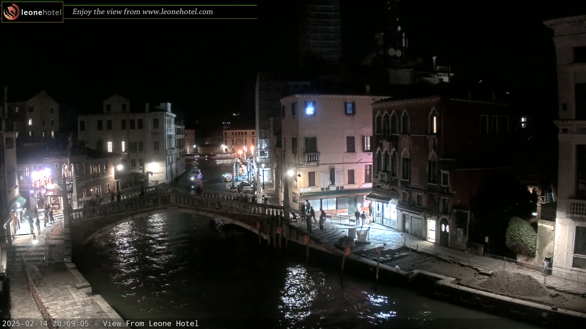 A nighttime view of a canal in Venice, Italy, shows several buildings lit up along the waterway and a bridge crossing the canal.
