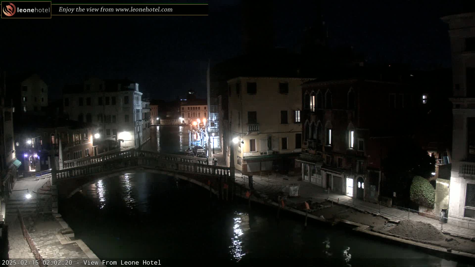 A nighttime view of a canal in Venice, Italy, showing a bridge, buildings lining the waterway, and calm water reflecting lights.